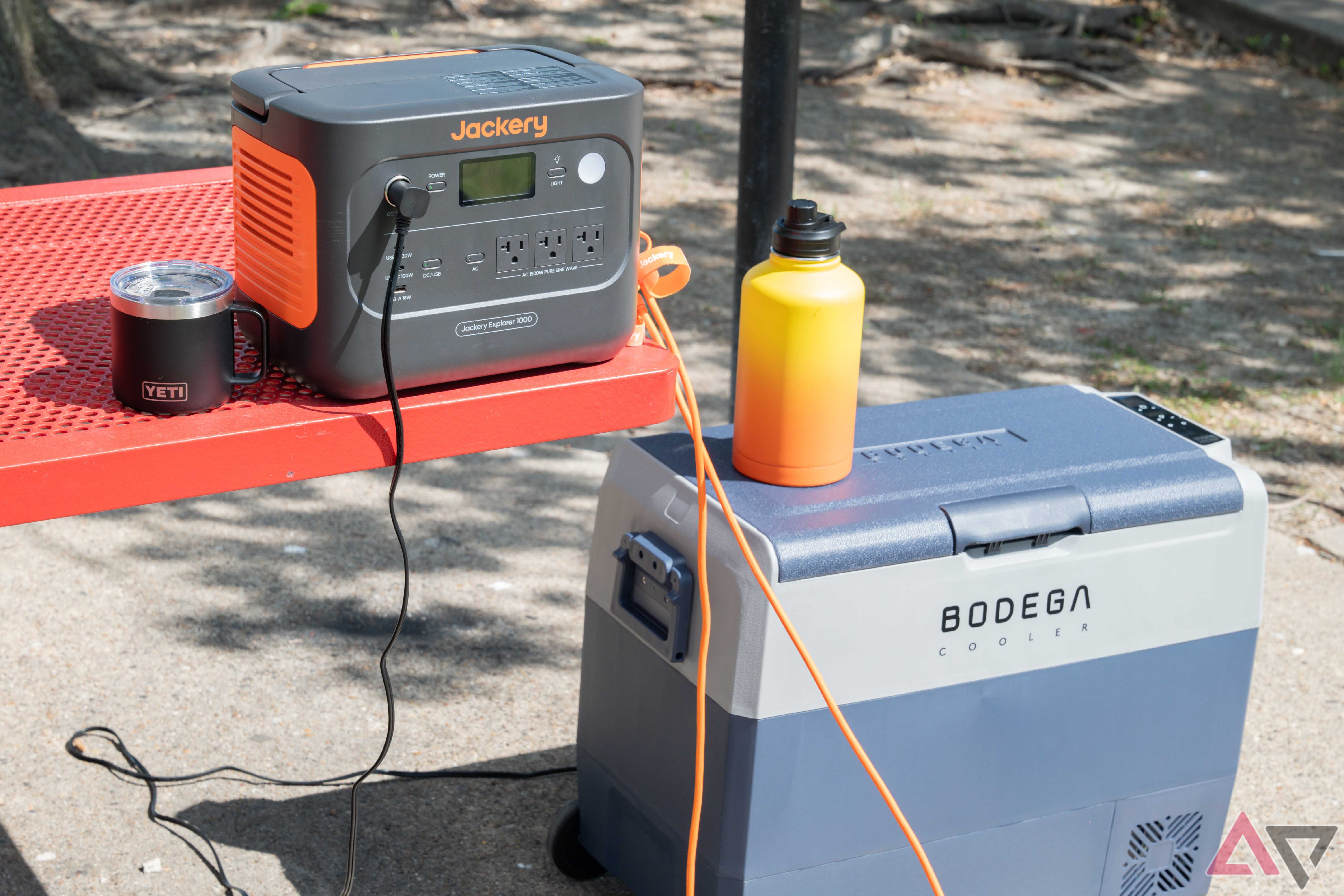 The Bodega Cooler car refrigerator is charged by a Jackery Explorer 1000 at a red picnic table.