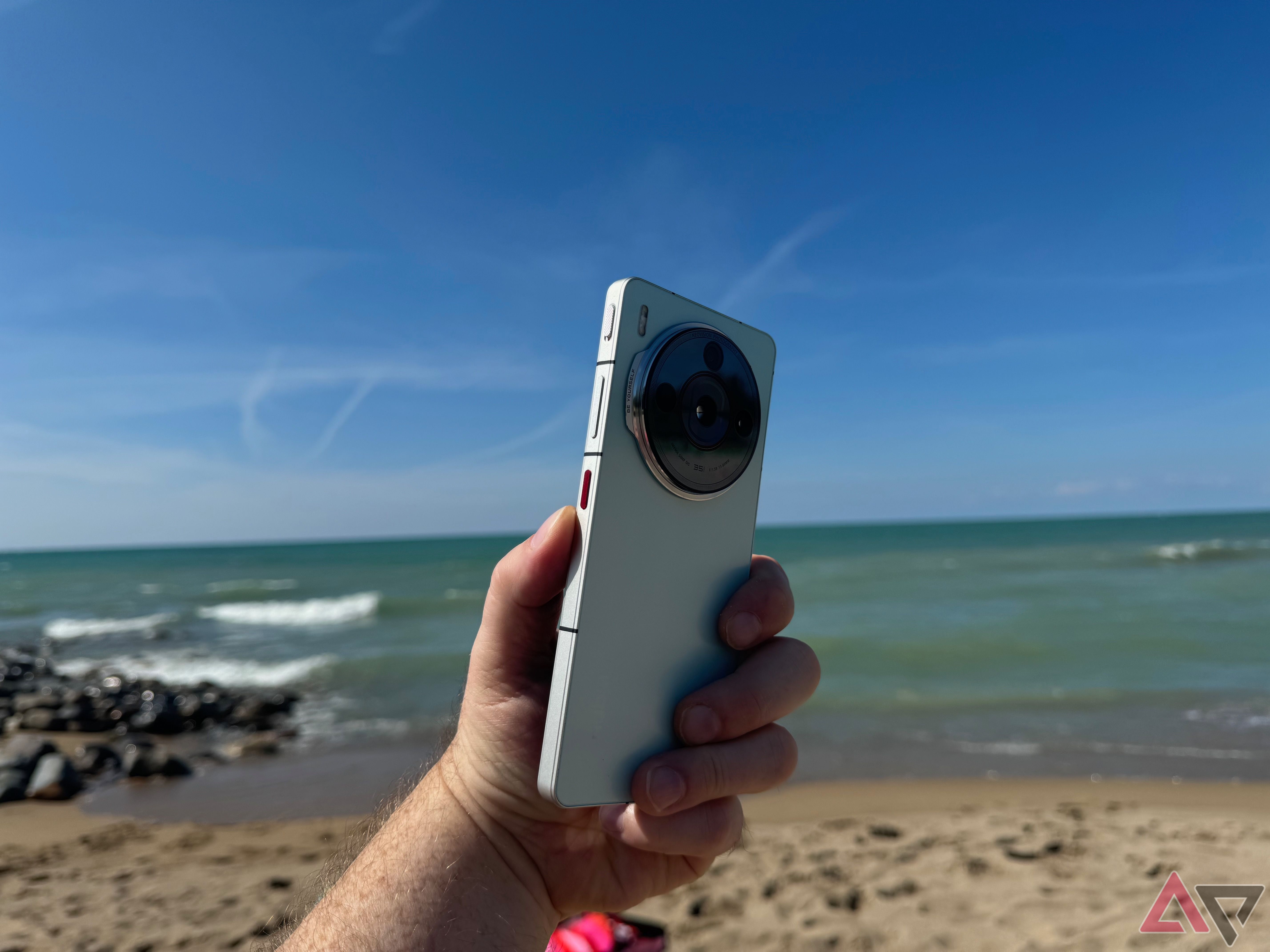 A hand holding a green Nubia Z60S Pro with a beach in the background.