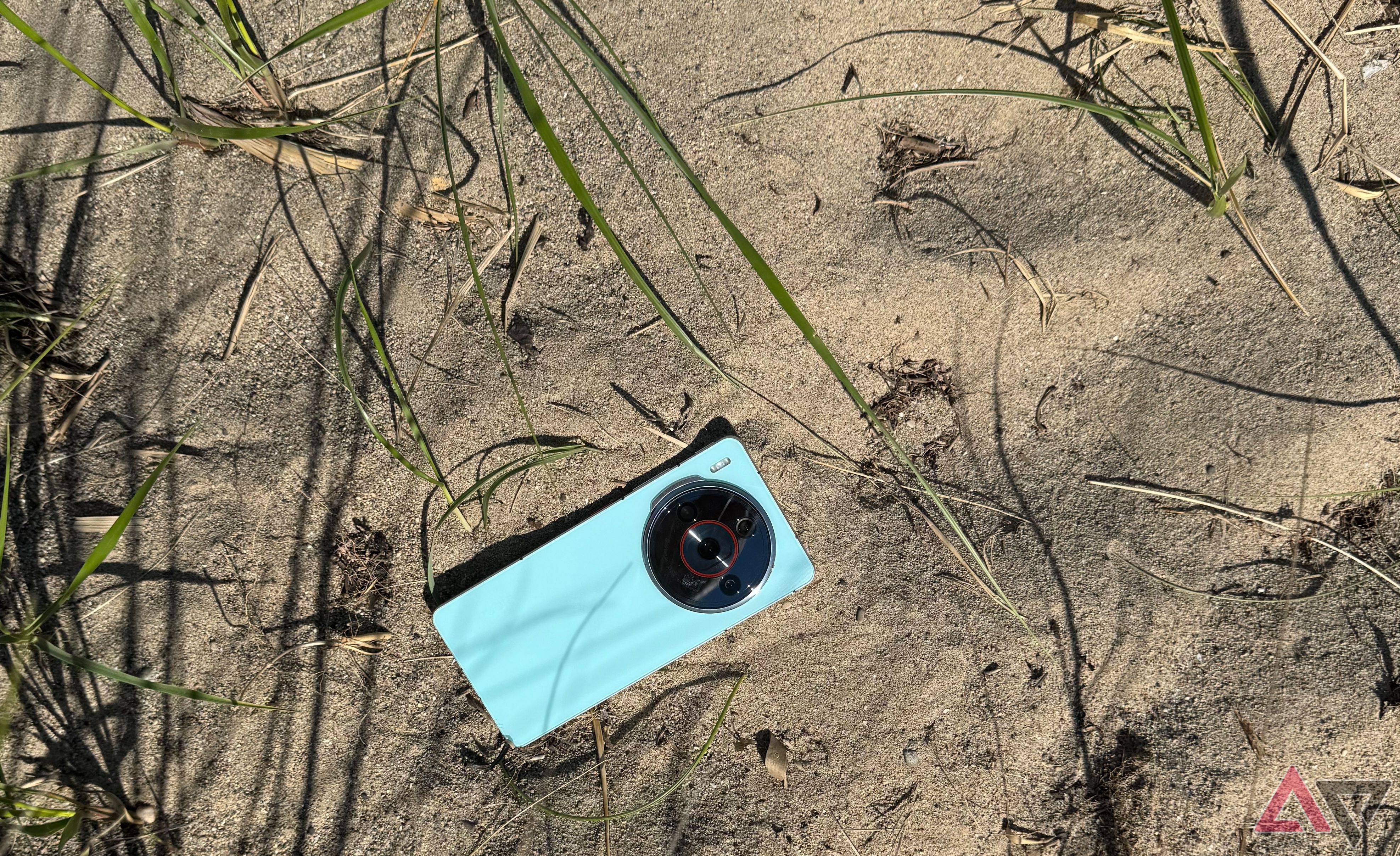 An aqua-colored Nubia Z60S Pro in the sand surrounded by beach grass.