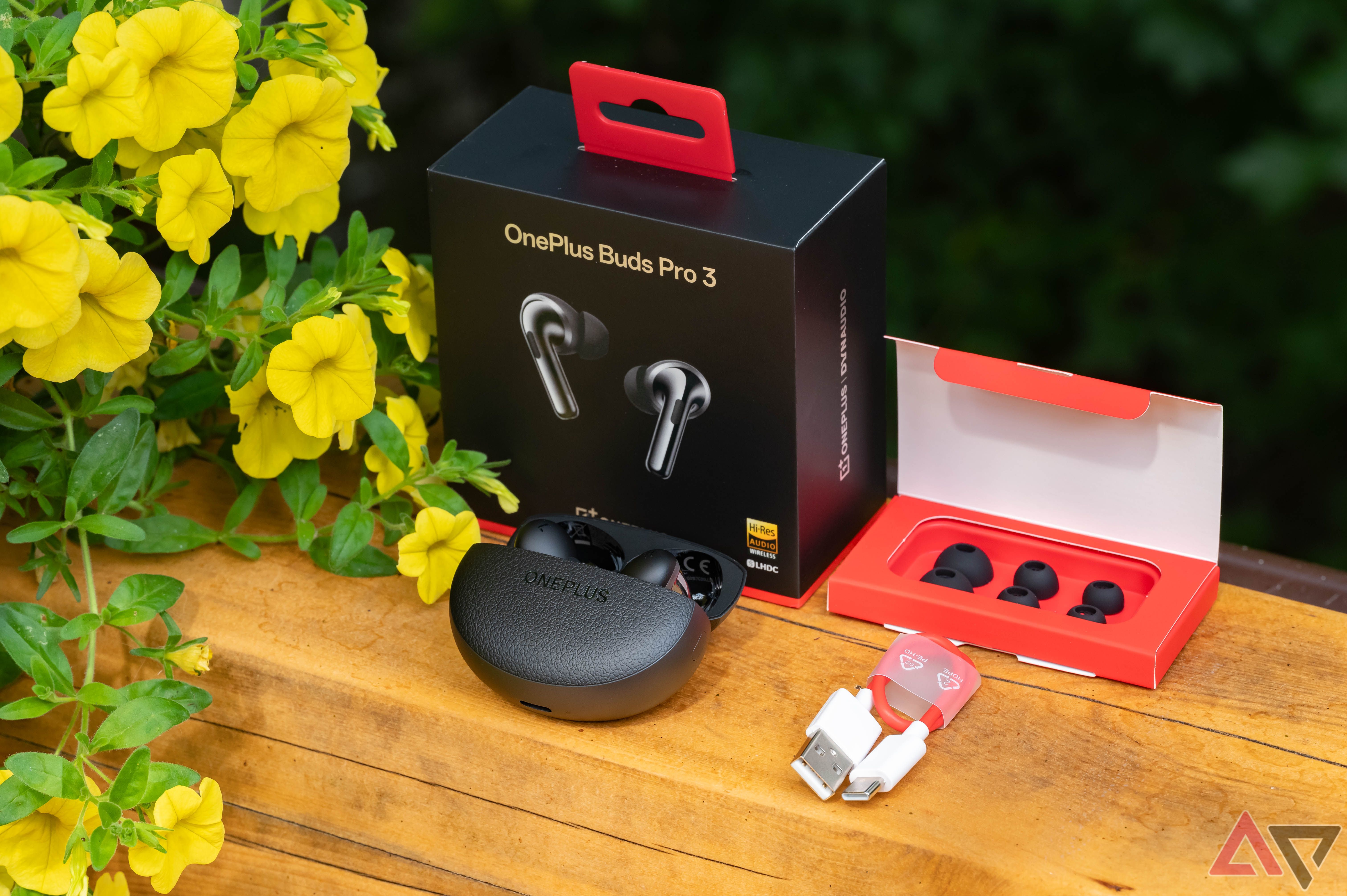 OnePlus Buds Pro 3 with box and accessories next to flowers