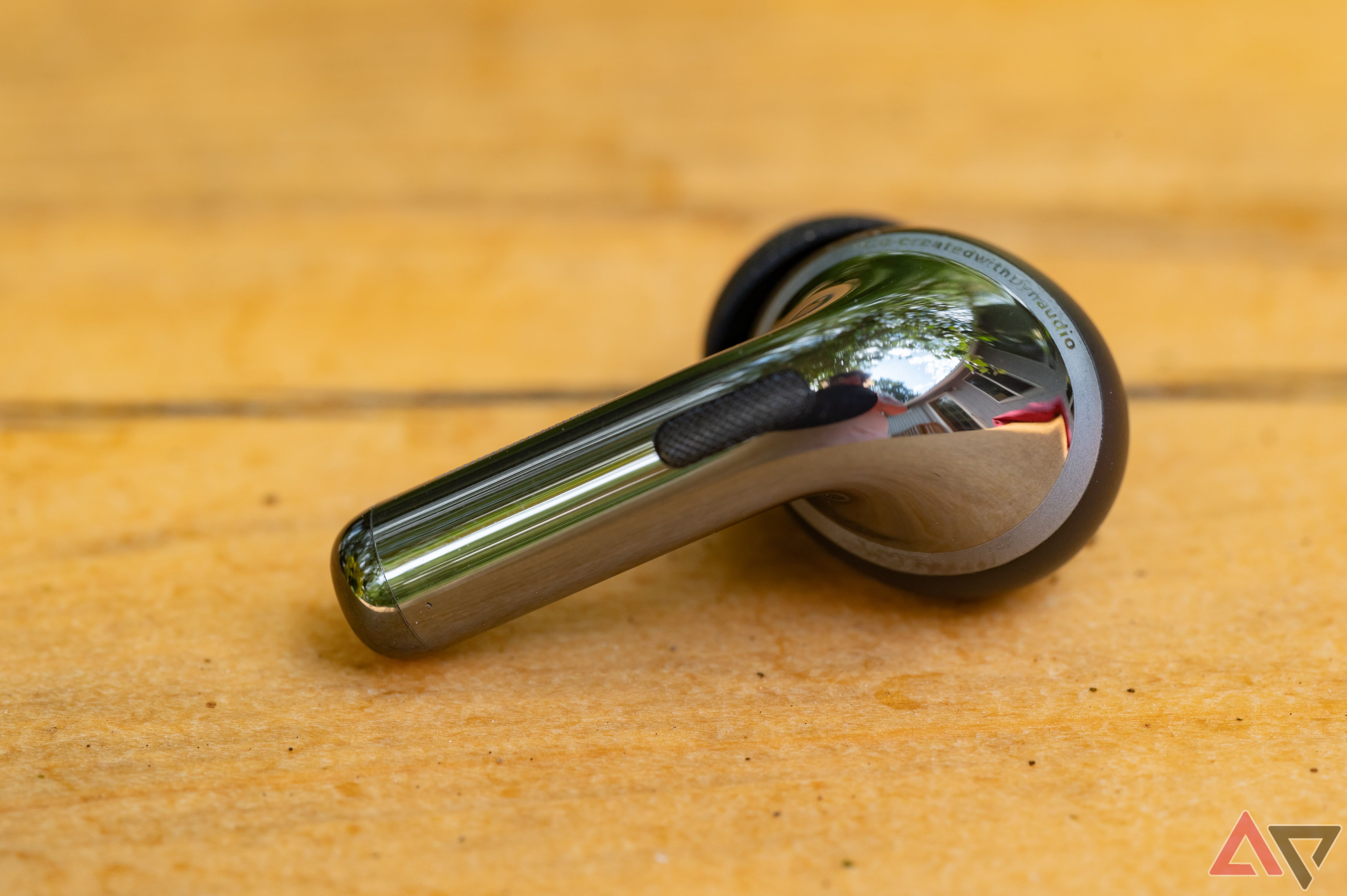 OnePlus Buds Pro 3 earbud, rear view on a wood surface