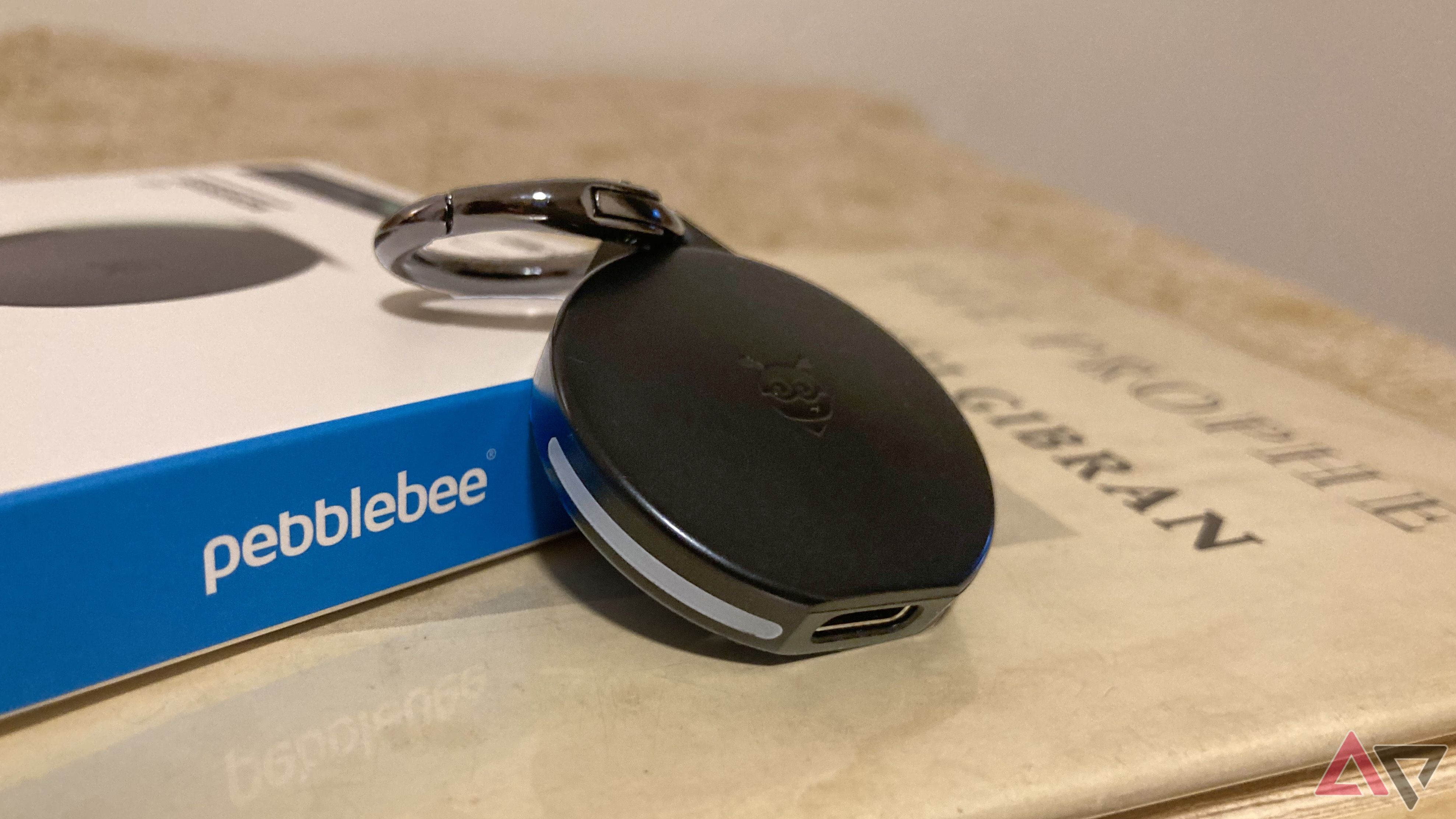 The Pebblebee Clip for Android leaning against its box while sitting on top of a book