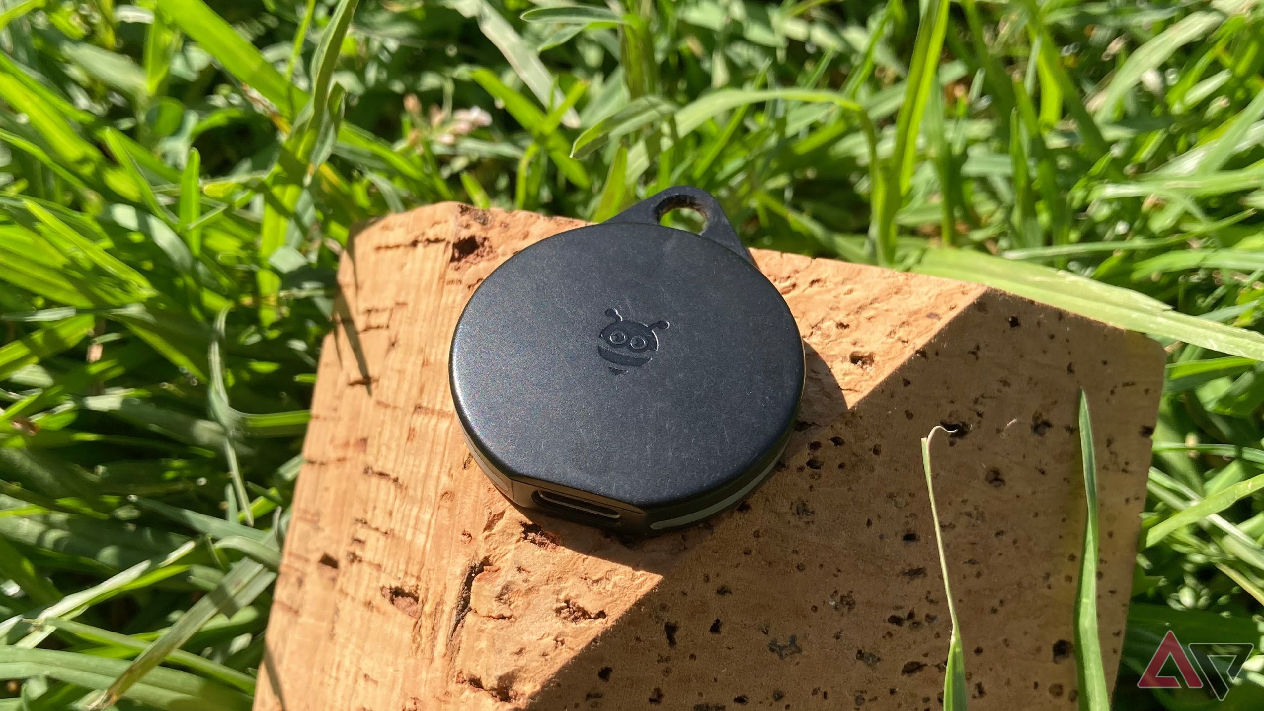 The Pebblebee Clip for Android sitting on the corner of a brick of cork in the grass