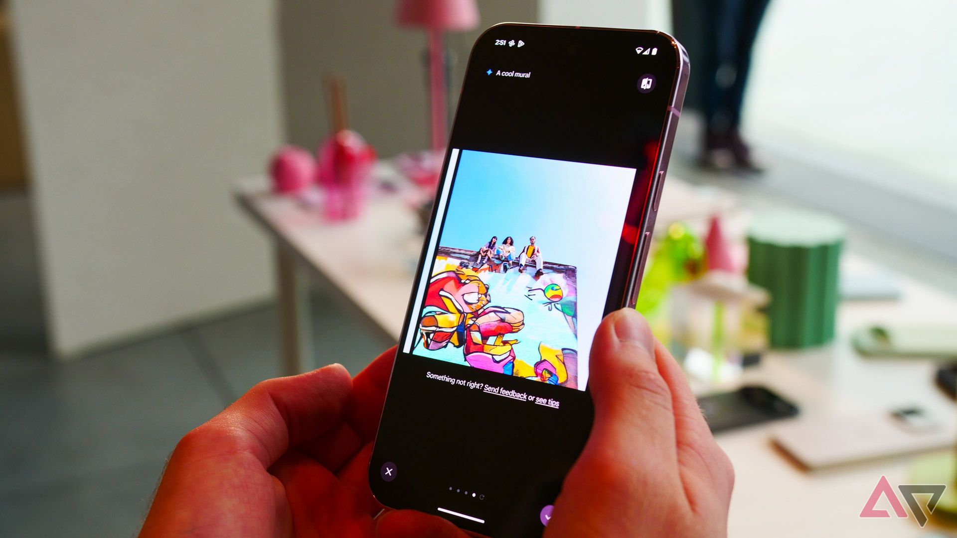 A person holding a smartphone displaying a photo of a colorful mural with people sitting on a ledge above it with text "a cool mural" on the top left of the screen