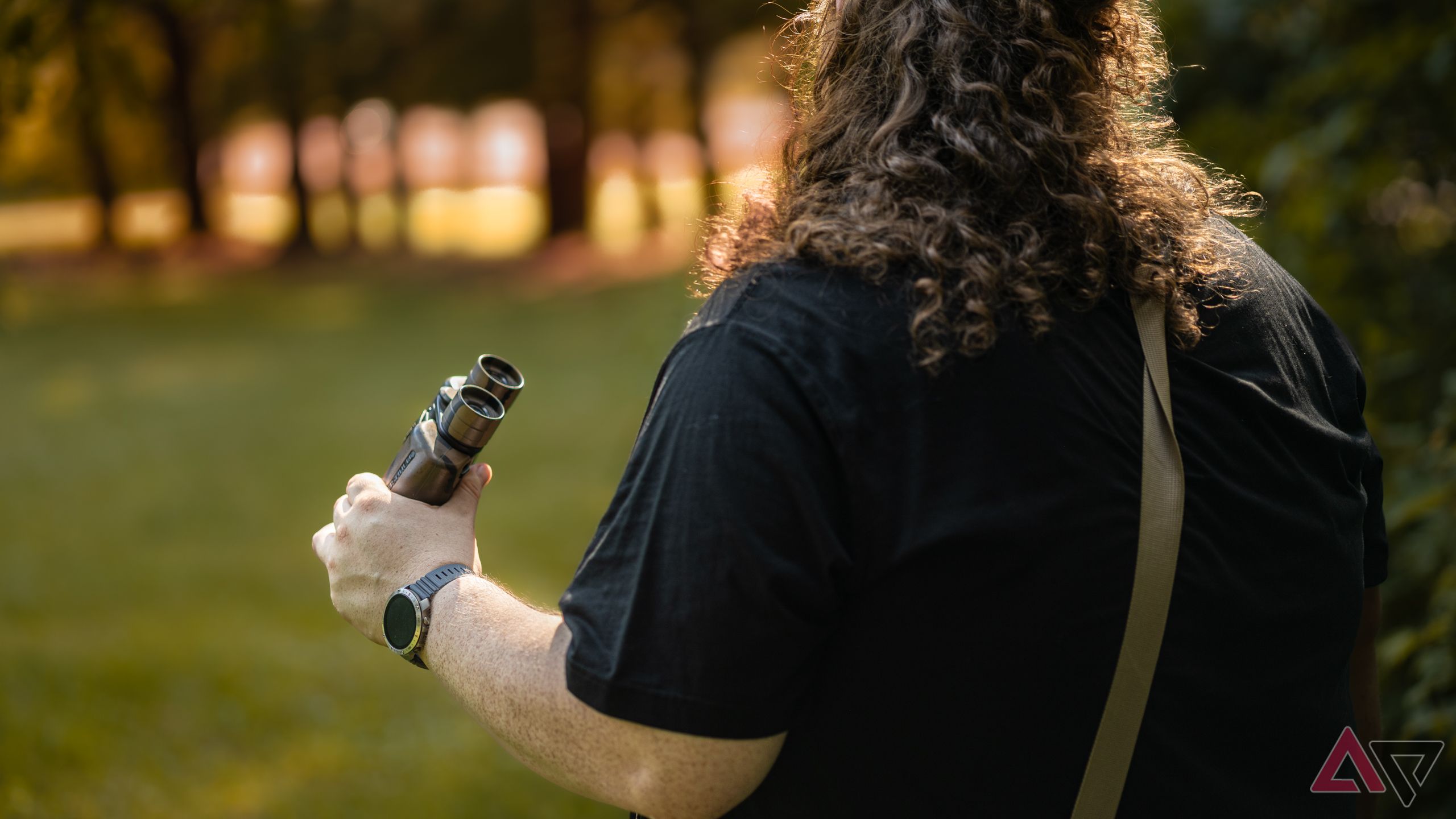 Back view of man looking into sunset while wearing Polar Grit X2 Pro smartwatch and using binoculars