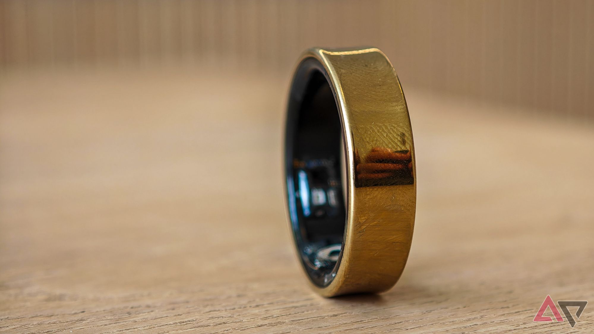 A gold Samsung Galaxy Ring resting on its side on a pale wooden table