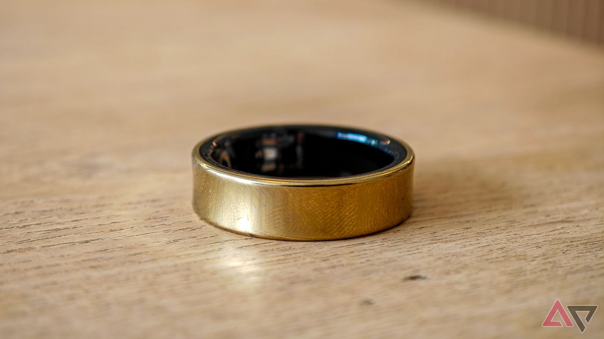 A gold Samsung Galaxy Ring lying on its side on a light wooden table