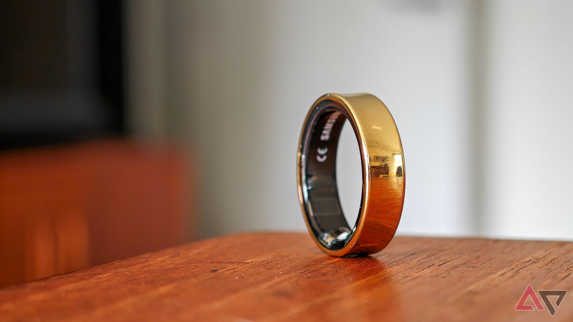 A gold Samsung Galaxy Ring resting vertically on the edge of a wooden table