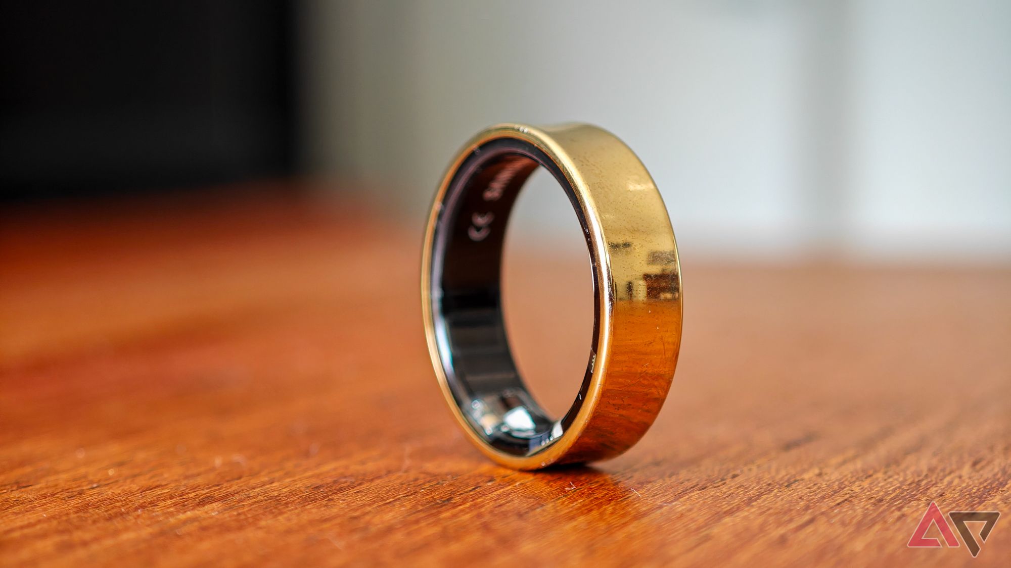 A gold Samsung Galaxy Ring resting vertically on a wooden table