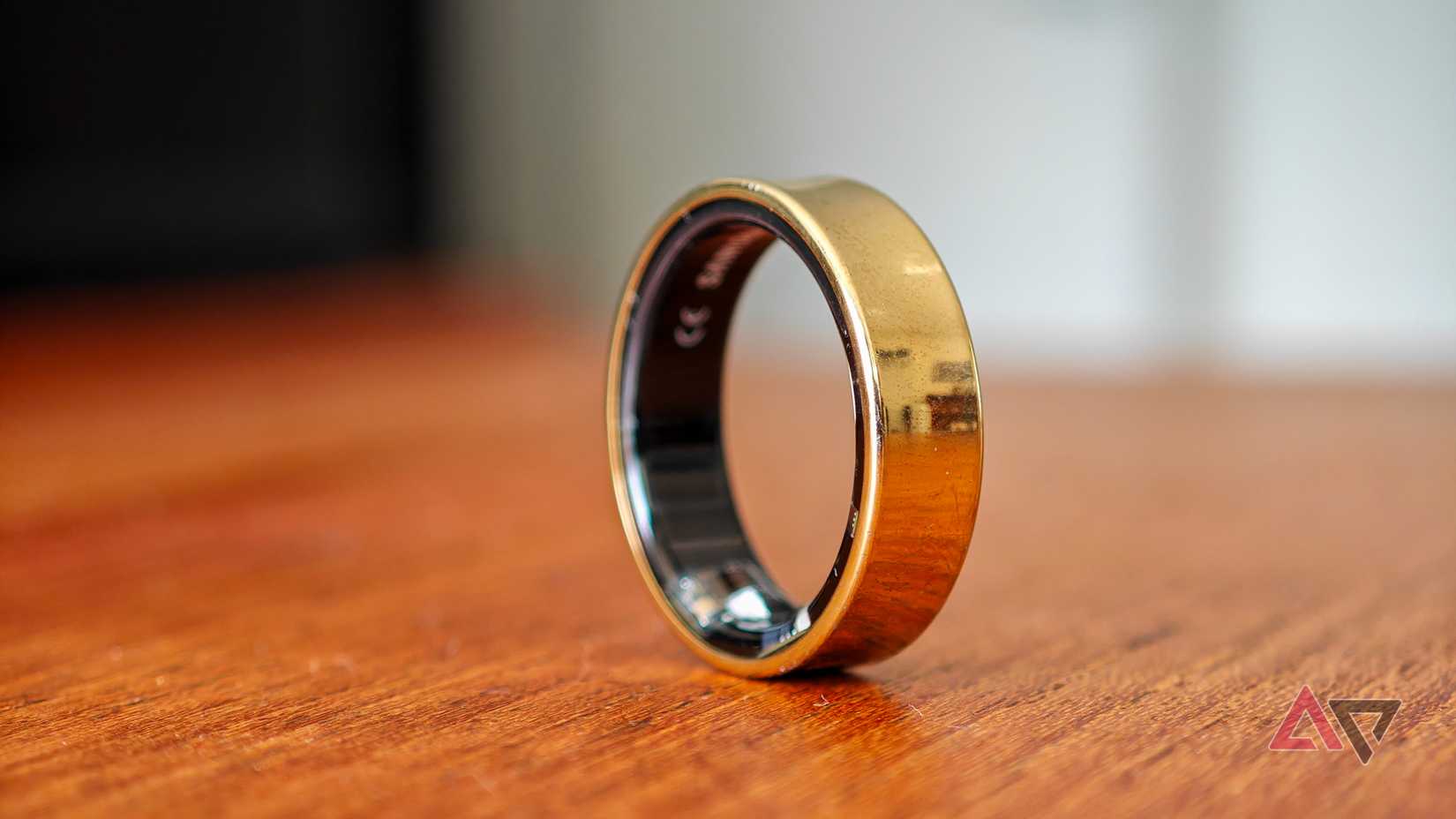 A gold Samsung Galaxy Ring resting vertically on a wooden table