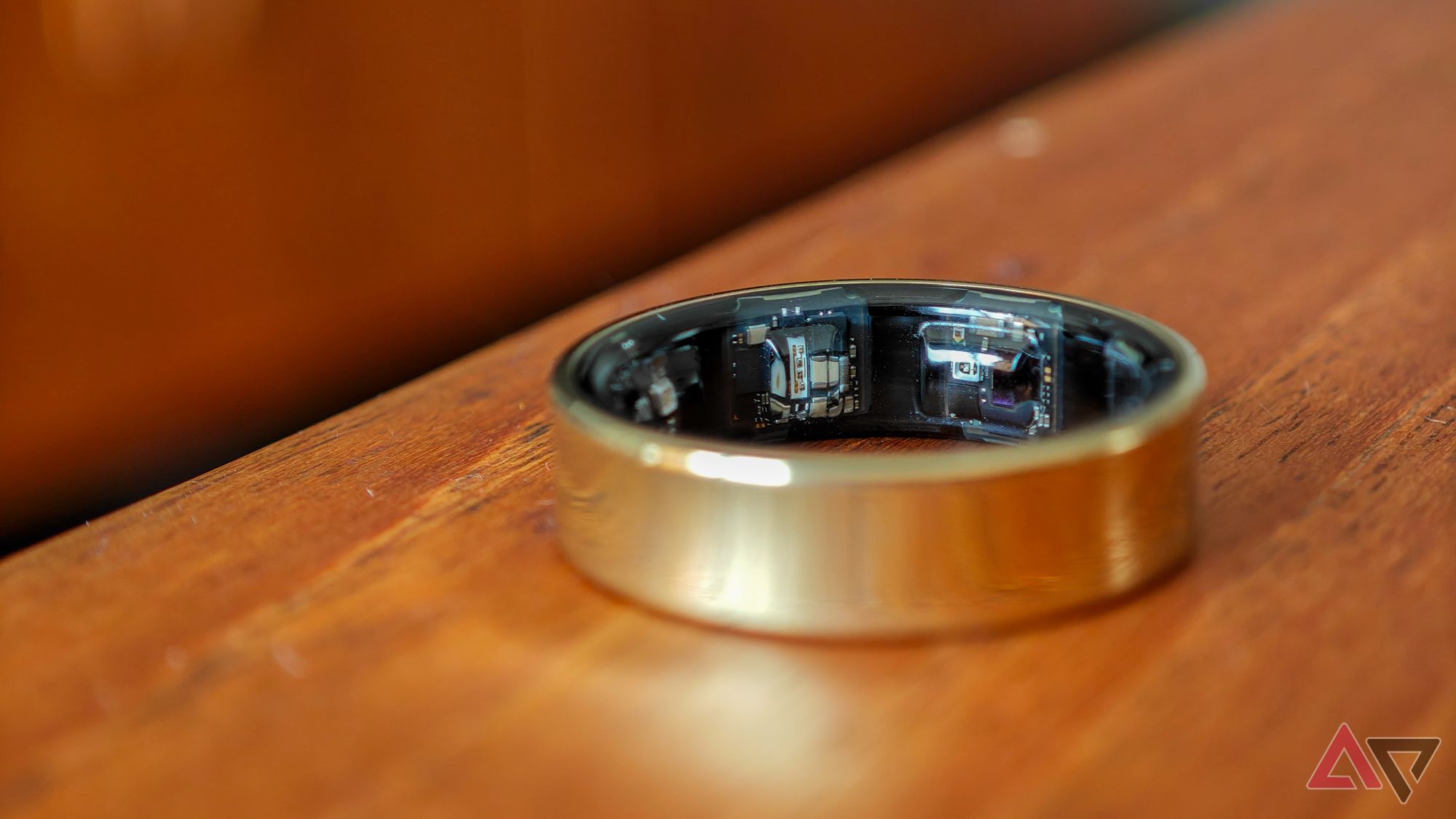 A gold Samsung Galaxy Ring lying on a wooden table with focus on the internal sensors