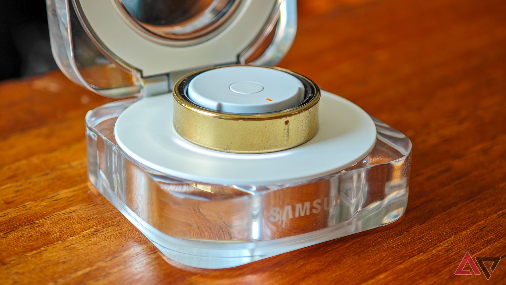 A gold Samsung Galaxy Ring resting in an open charging case, with the charging LED ring active