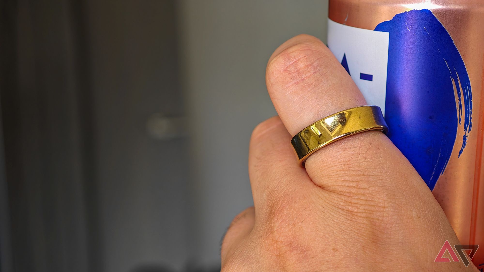 A gold Samsung Galaxy Ring on someone's index finger as they hold a canned drink