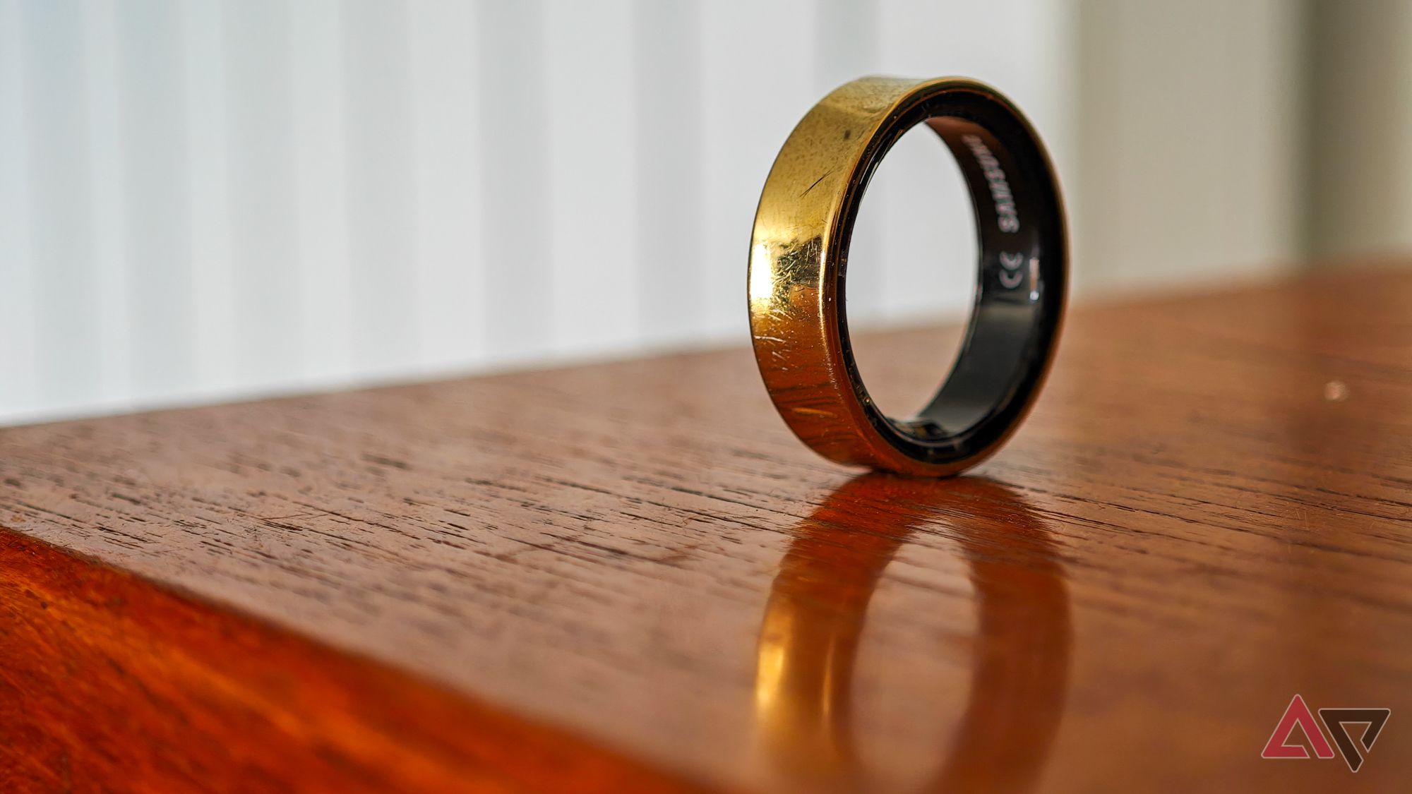 A gold Samsung Galaxy Ring resting on its edge on a wooden surface