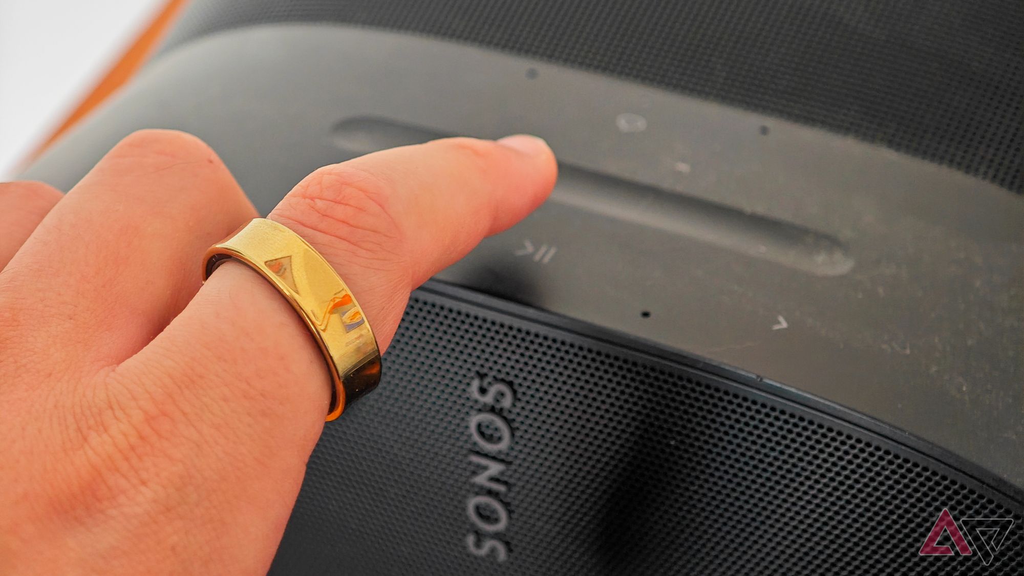 A gold Samsung Galaxy Ring on an index finger using a Sonos speaker