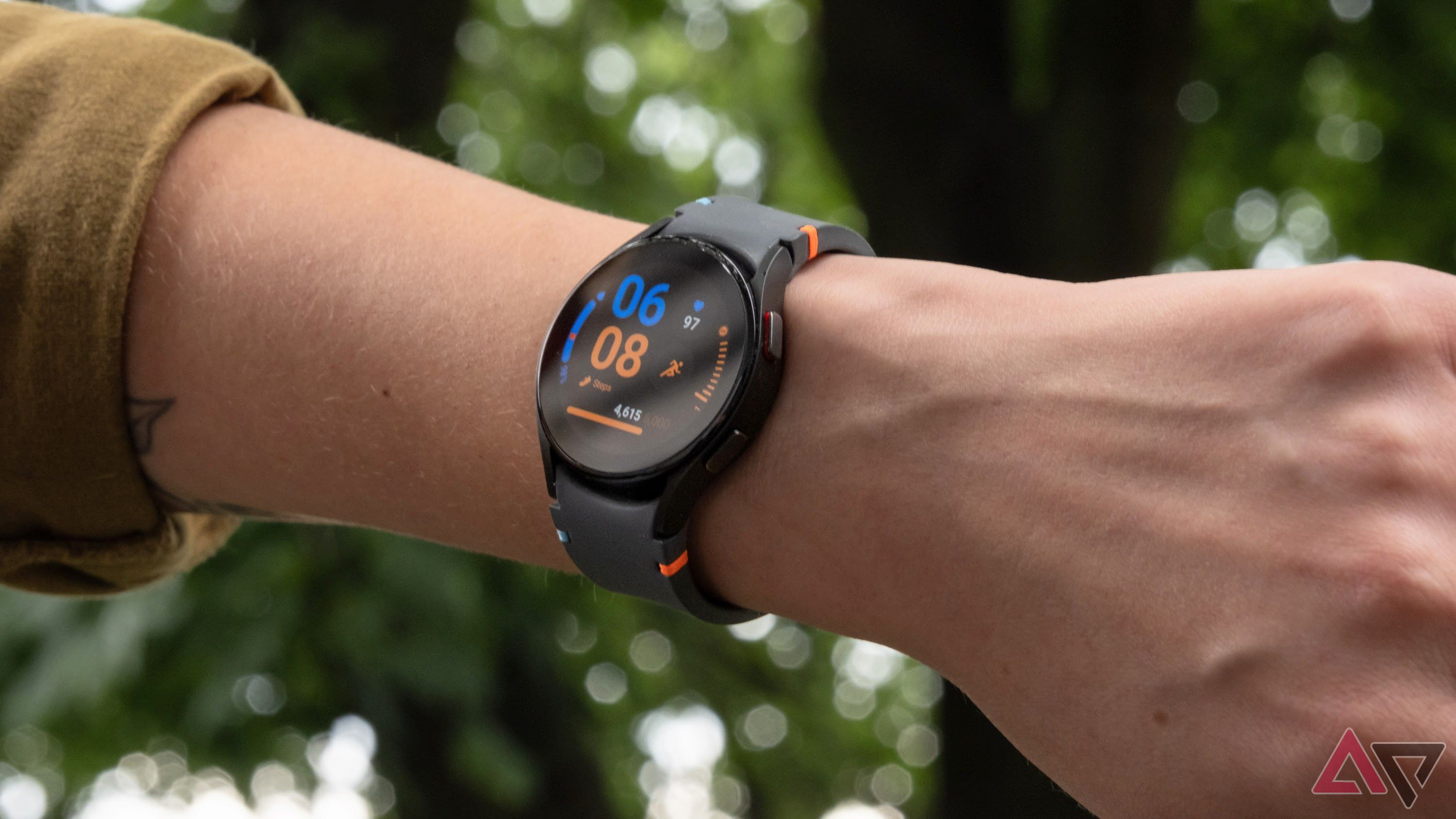 The Samsung Galaxy Watch FE on an arm in front of foliage.