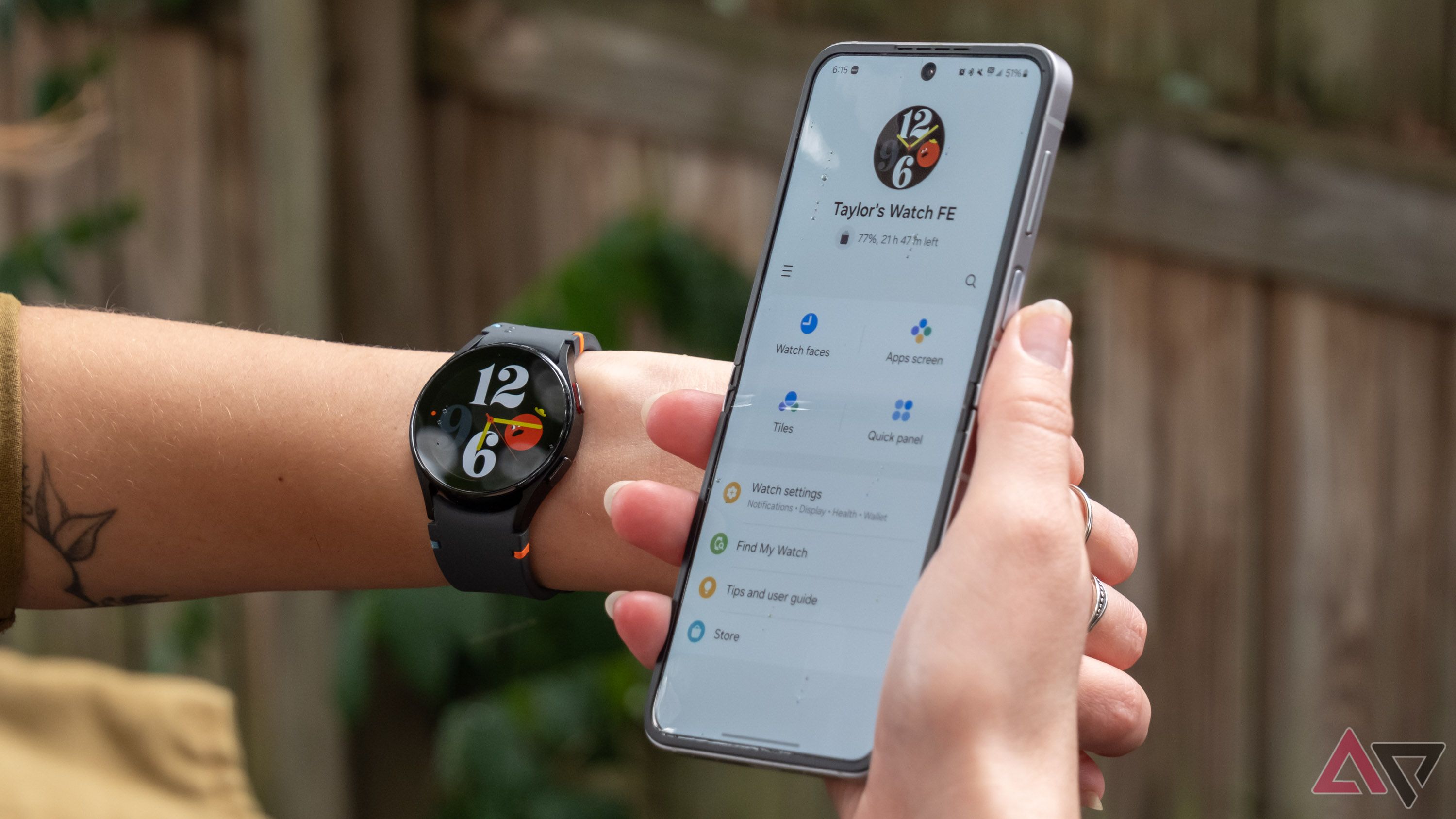 A Samsung Galaxy Watch FE on the wrist next to a Samsung Galaxy Z Flip 6 is displaying the Galaxy Wearable app.