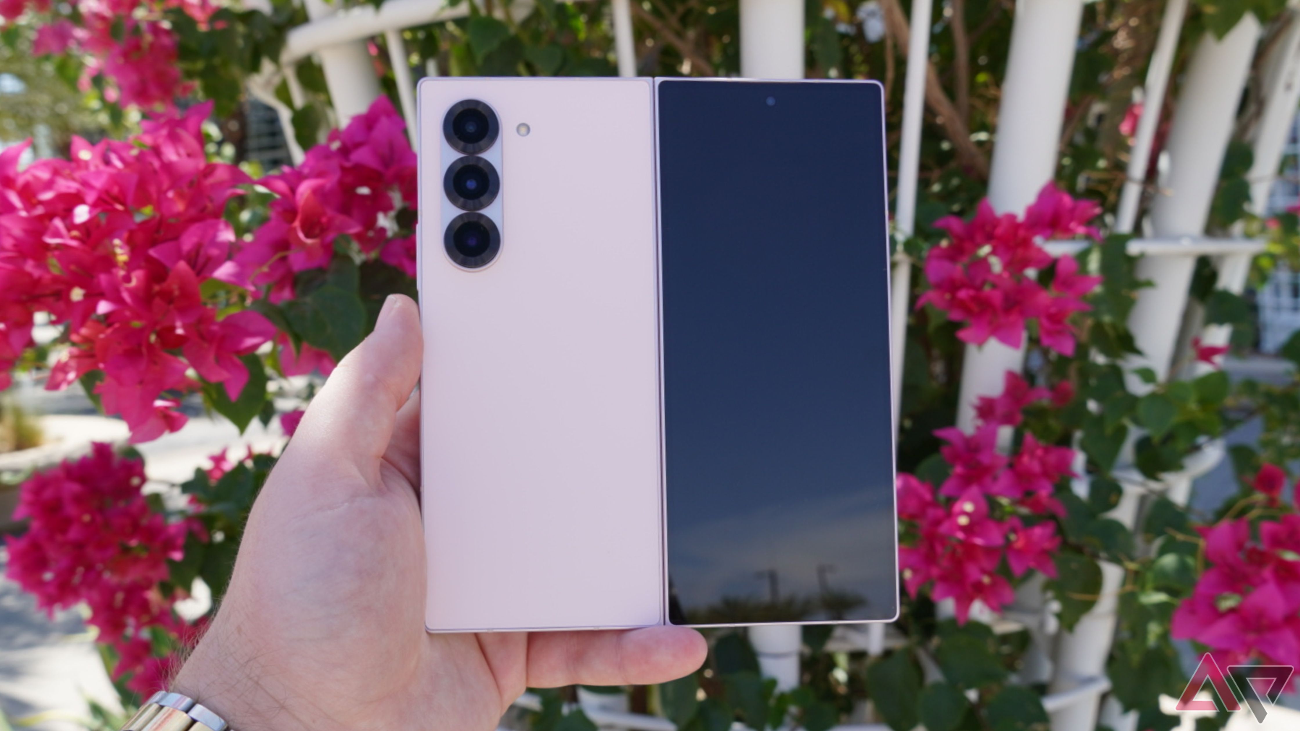 The pink Samsung Galaxy Z Fold 6 in the hand in front of pink flowers.