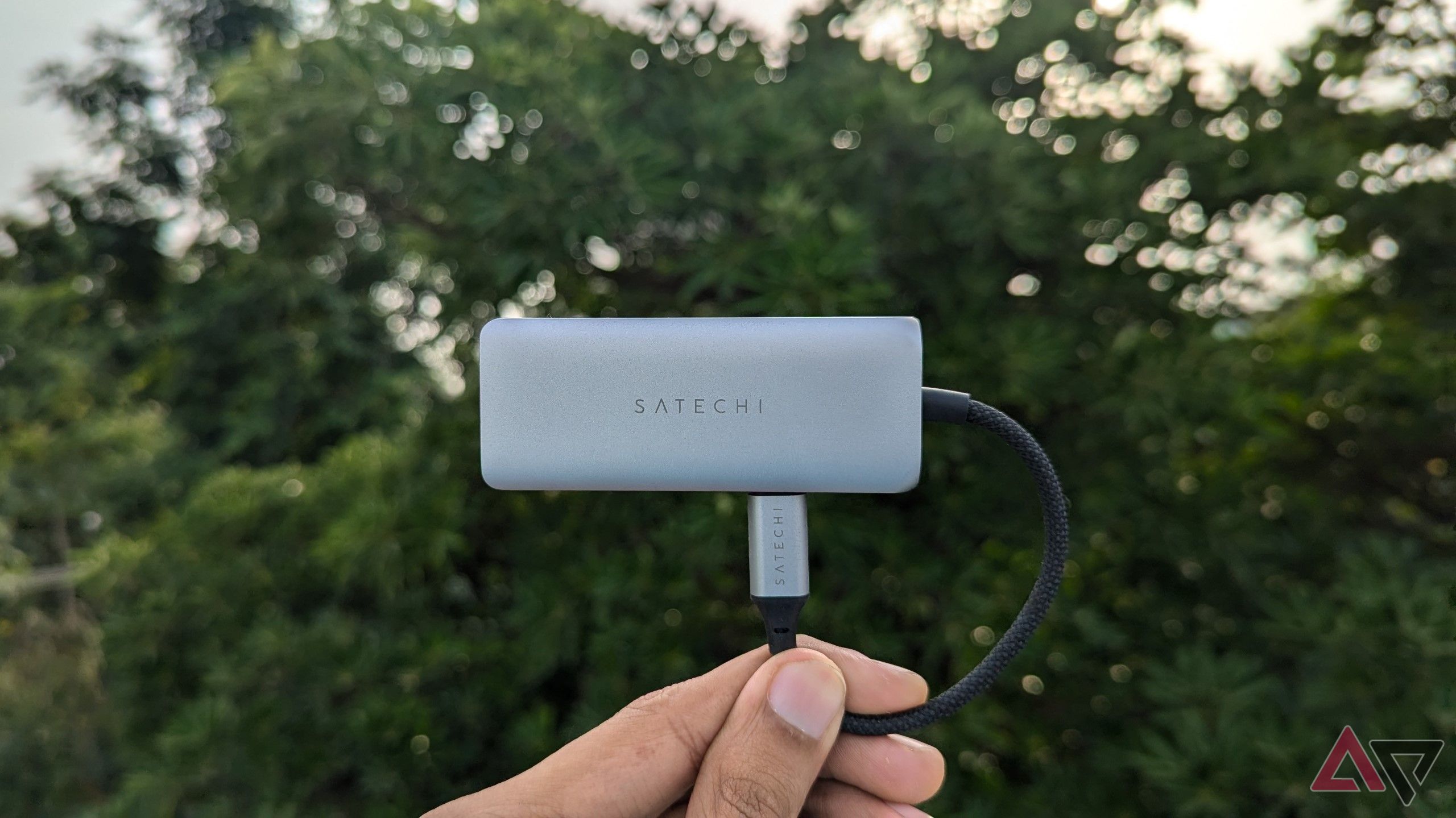 Silver-gray USB hub with its cable plugged into itself held against a tree in the backgrounds