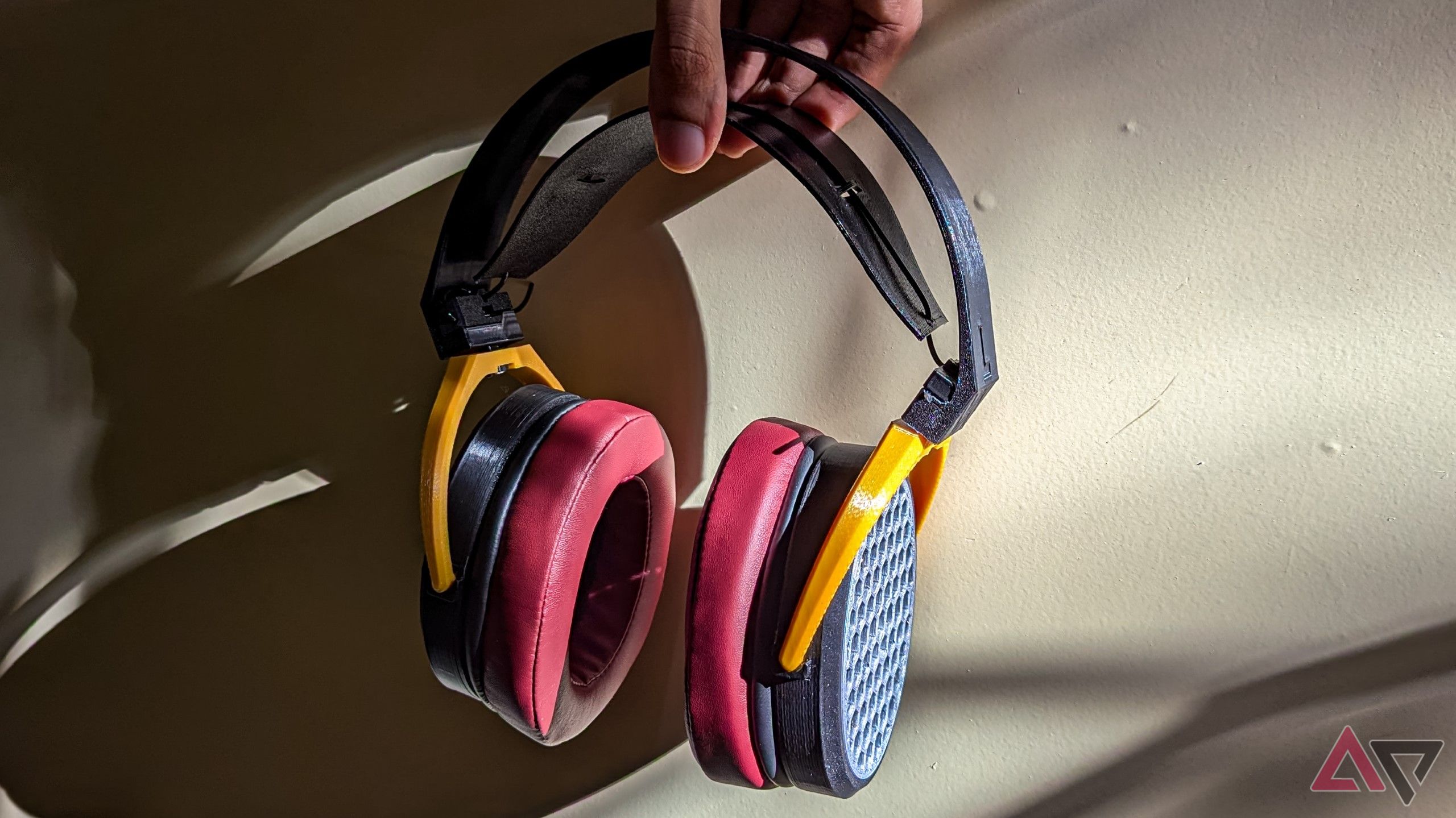 Open-back headphones held against a wall with sunlight casting a big shadow of the headphones in half the frame