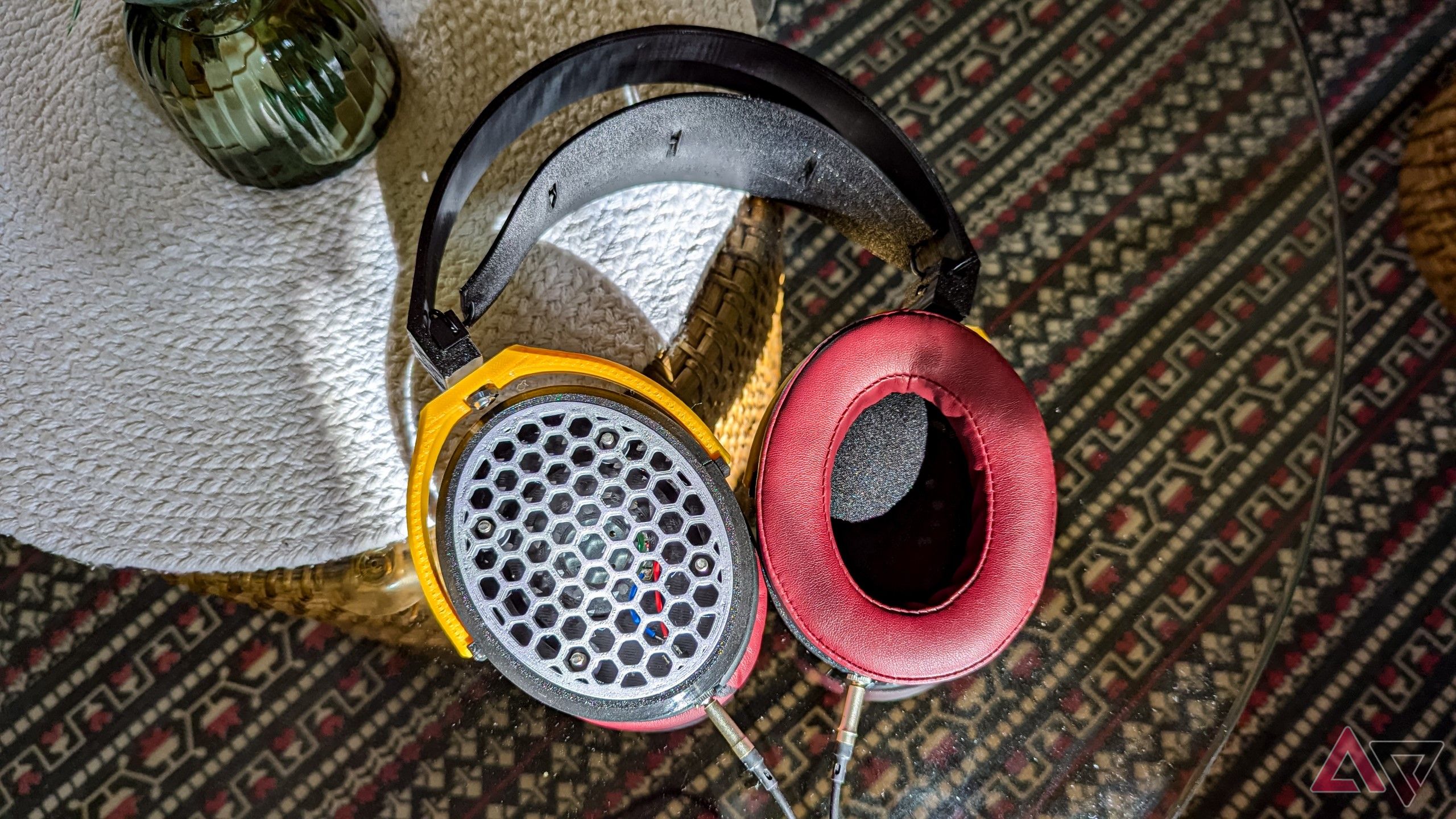 open-back headphones on a glass table with a round white woven mat and a woven blue and white carpet seen on the floor