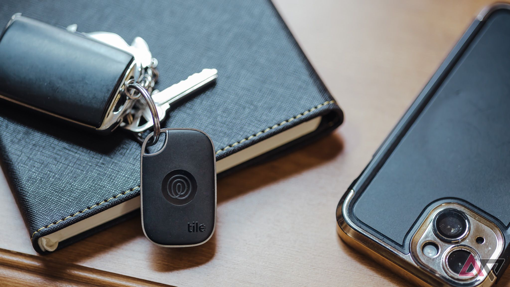 Tile Pro 2024 tracker on keyring next to black notebook and smartphone