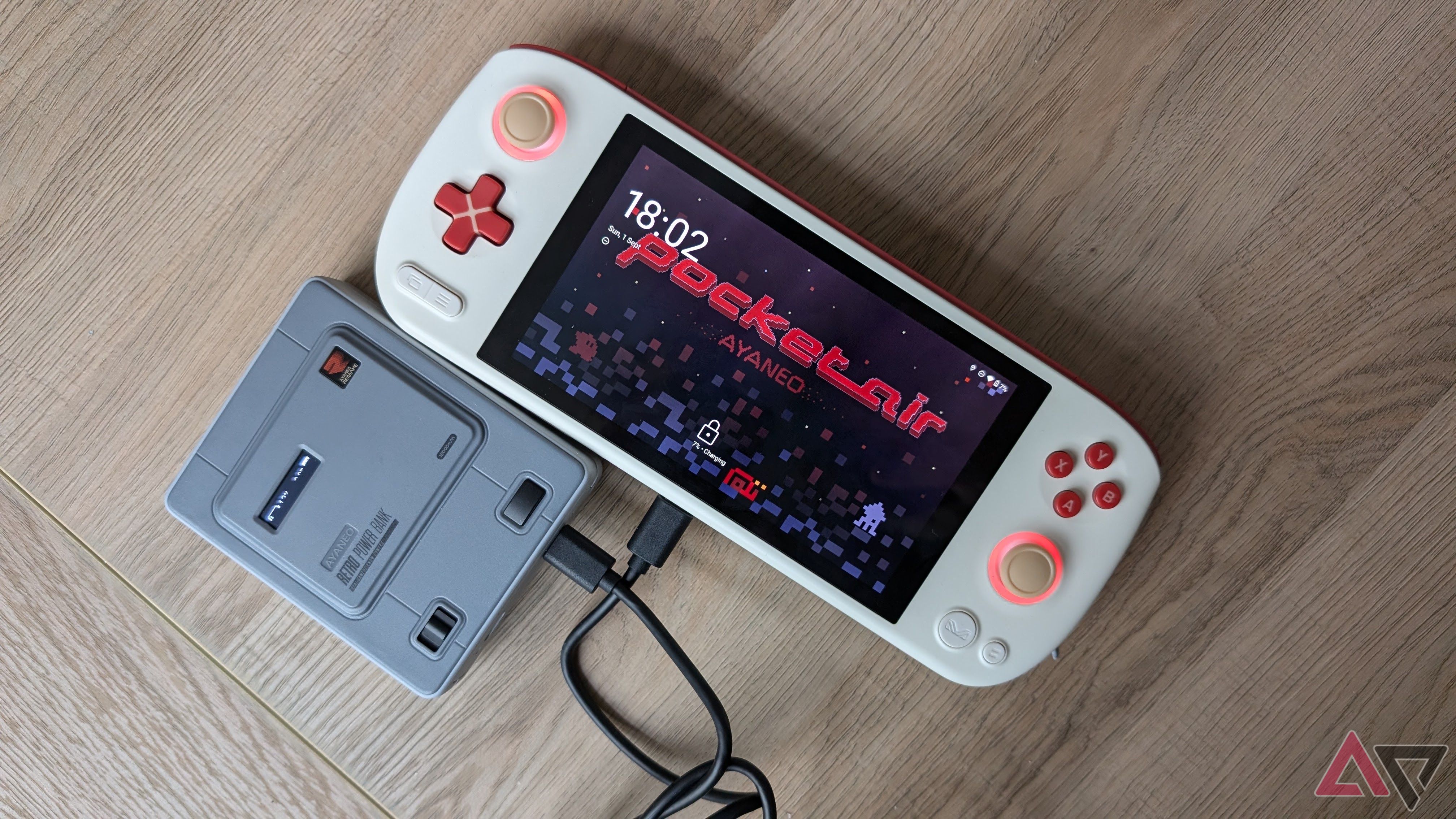 Ayaneo retro power bank next to a white handheld console on a light wooden surface