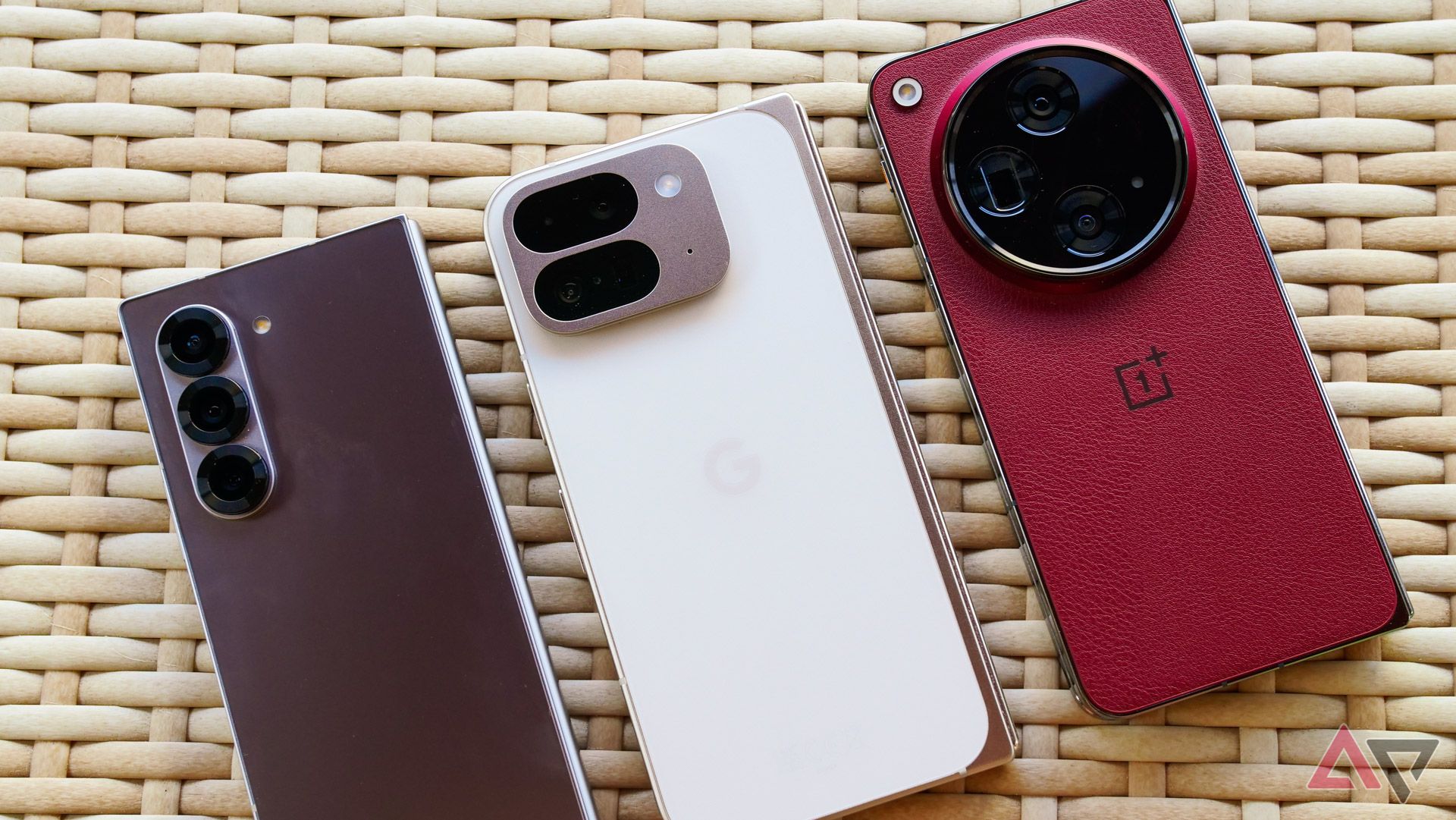 The Google Pixel 9 Pro Fold next to the Galaxy Z Fold 6 and OnePlus Open on a wicker table.