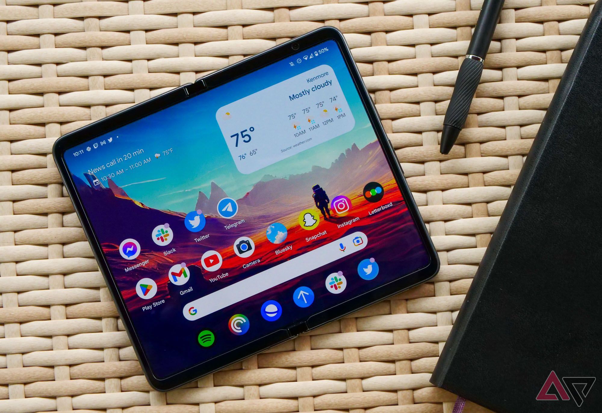 The Google Pixel Fold on a wicker table with a notebook and pen next to it.