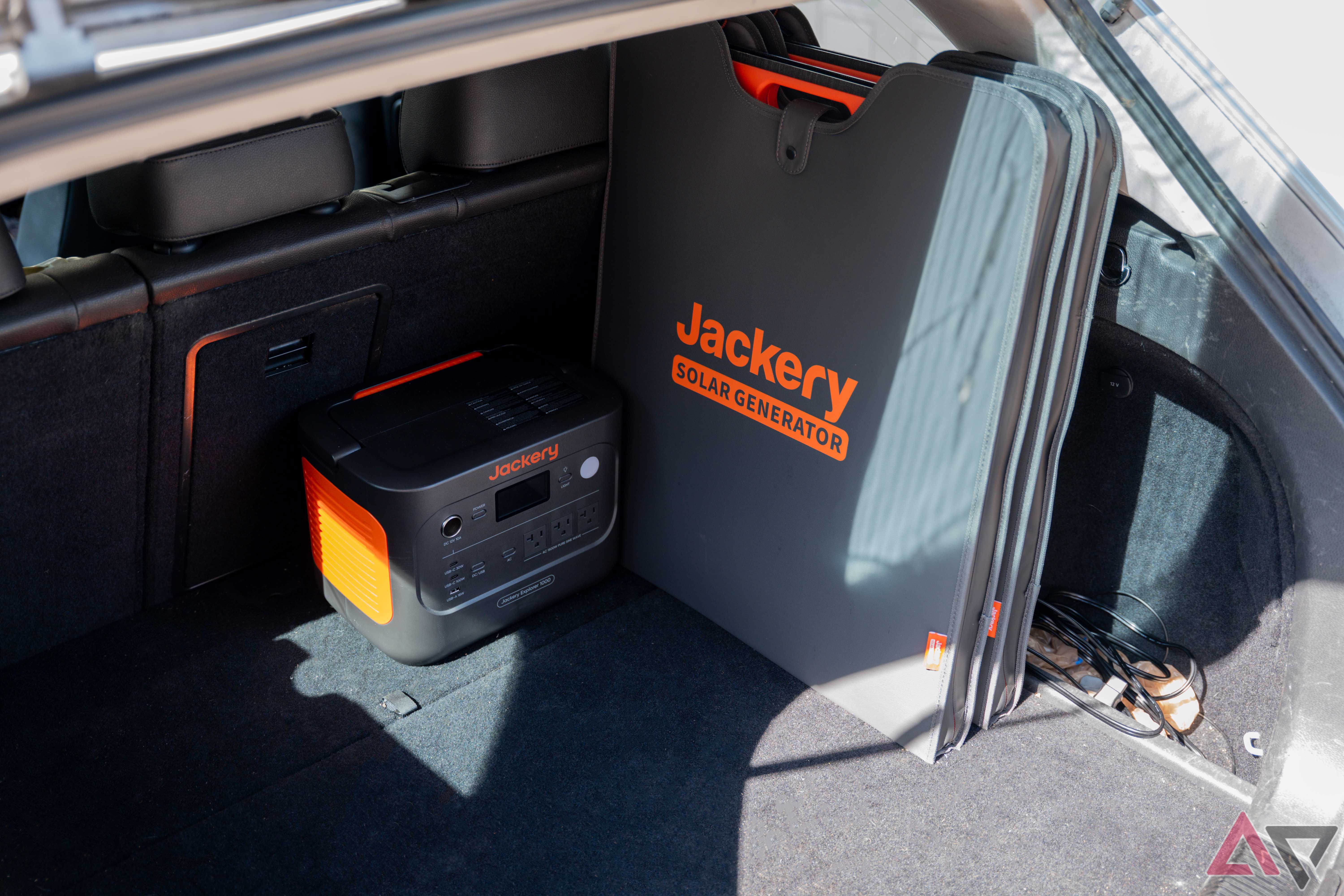 A three quarter view of the Jackery Explorer 1000 v2 in the back of a station wagon with two 200W solar panels.