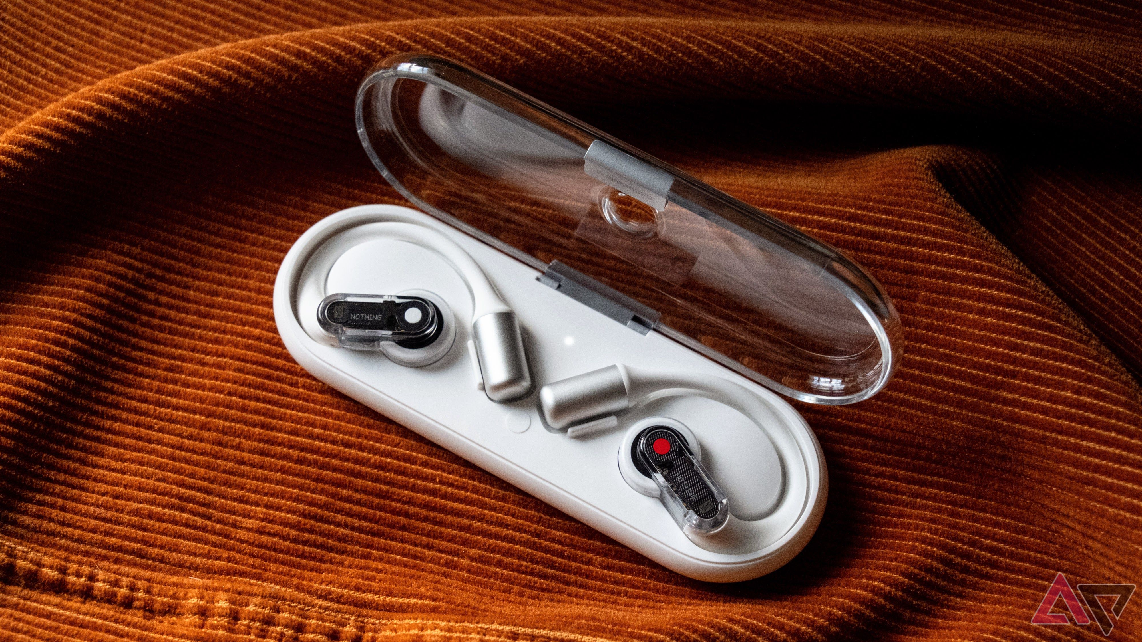 Earbuds in a case on an orange backdrop.