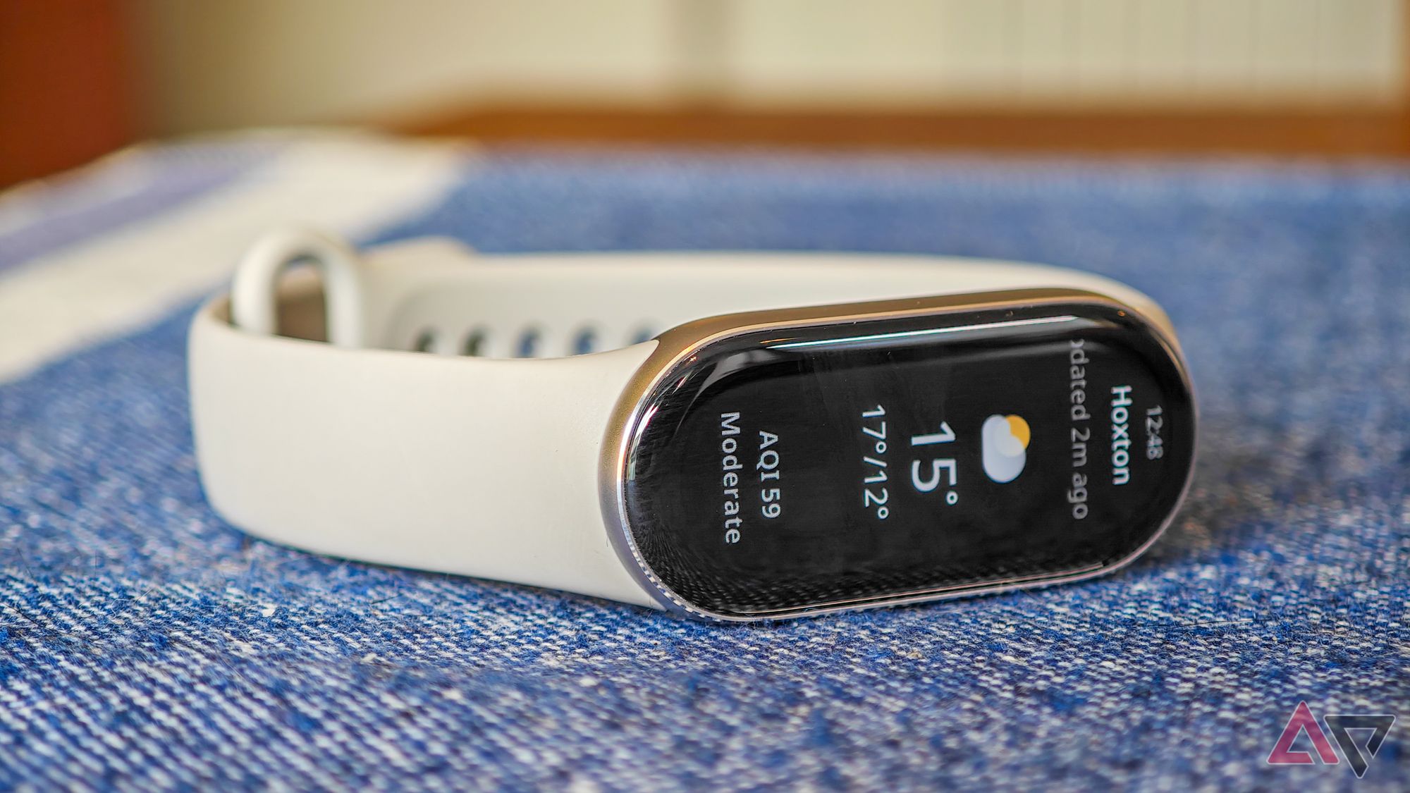 Xiaomi Smart Band 9 lying on a blue tablecloth showing the weather