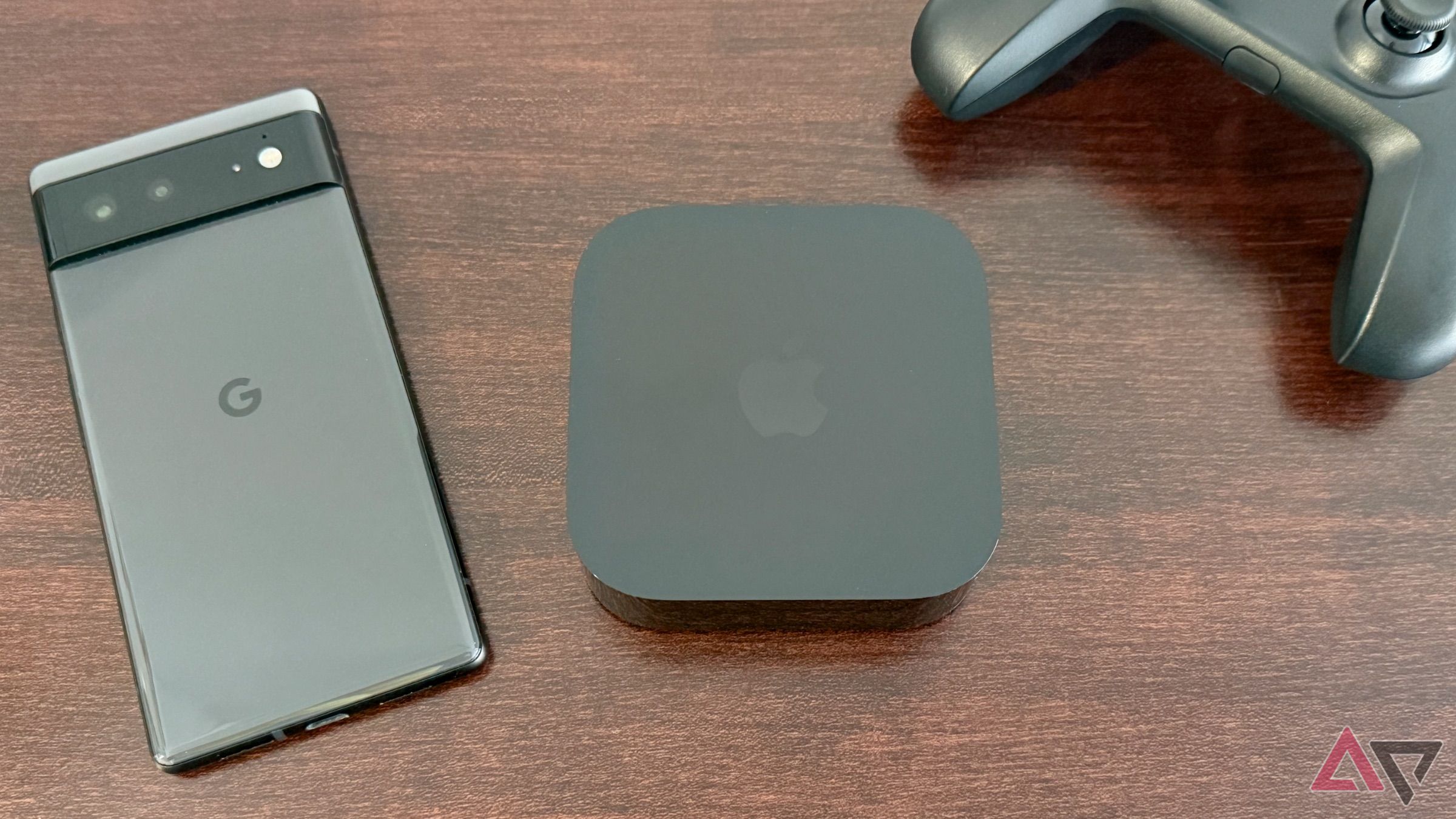 Apple TV 4K trên bàn gỗ tối màu bên cạnh bộ điều khiển trò chơi Google Pixel 6 và Nimbus