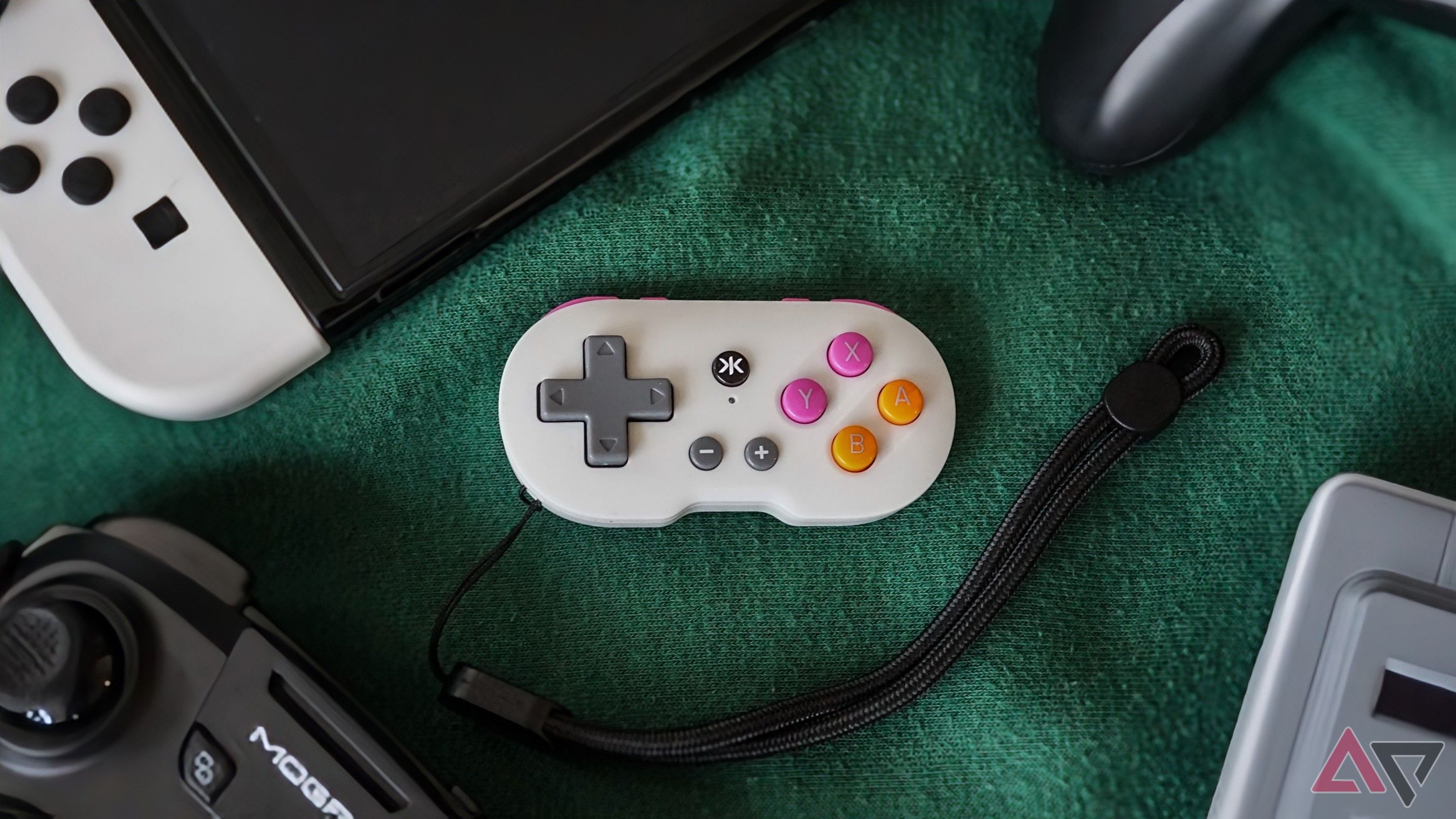 grey Atom controller resting on green fabric surrounded by gaming accessories