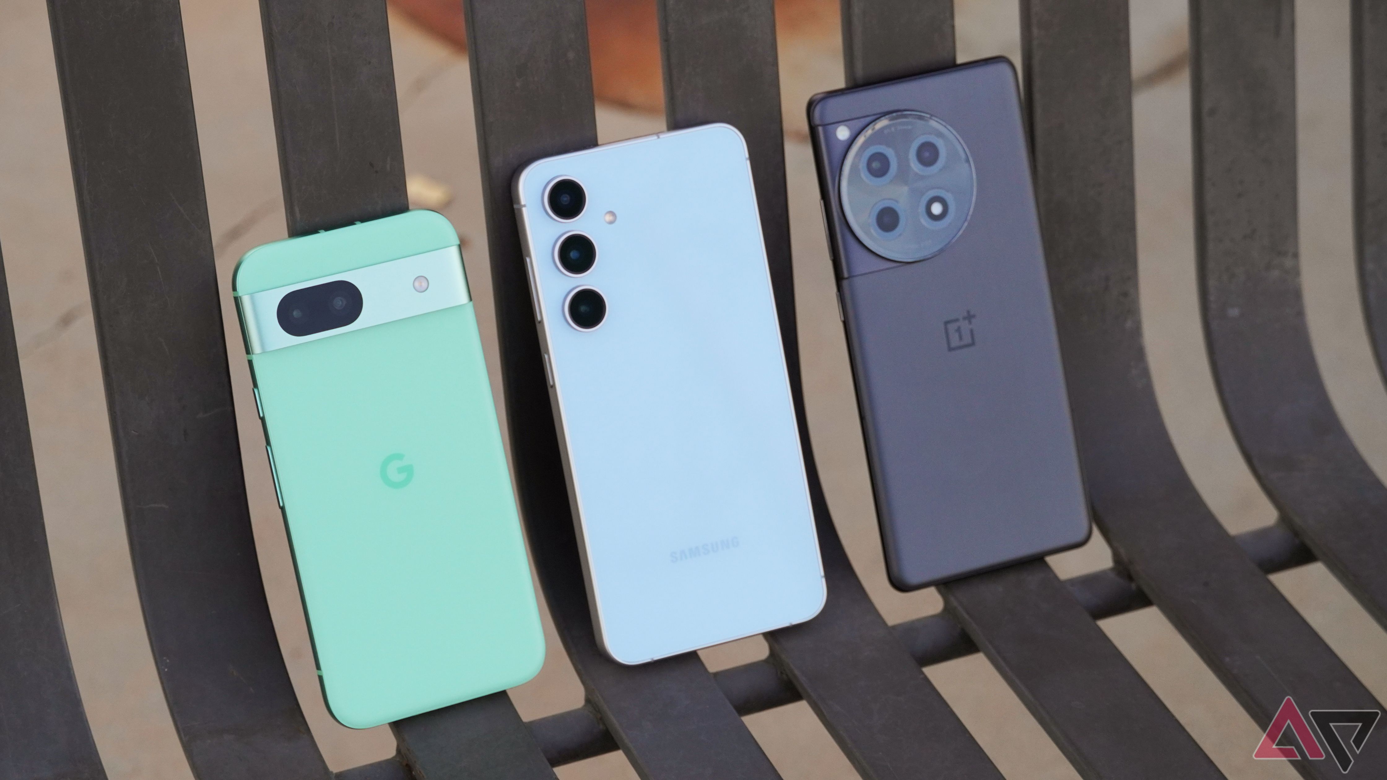 Google Pixel 8a, Galaxy S24 FE, and OnePlus 12R placed on the bench.