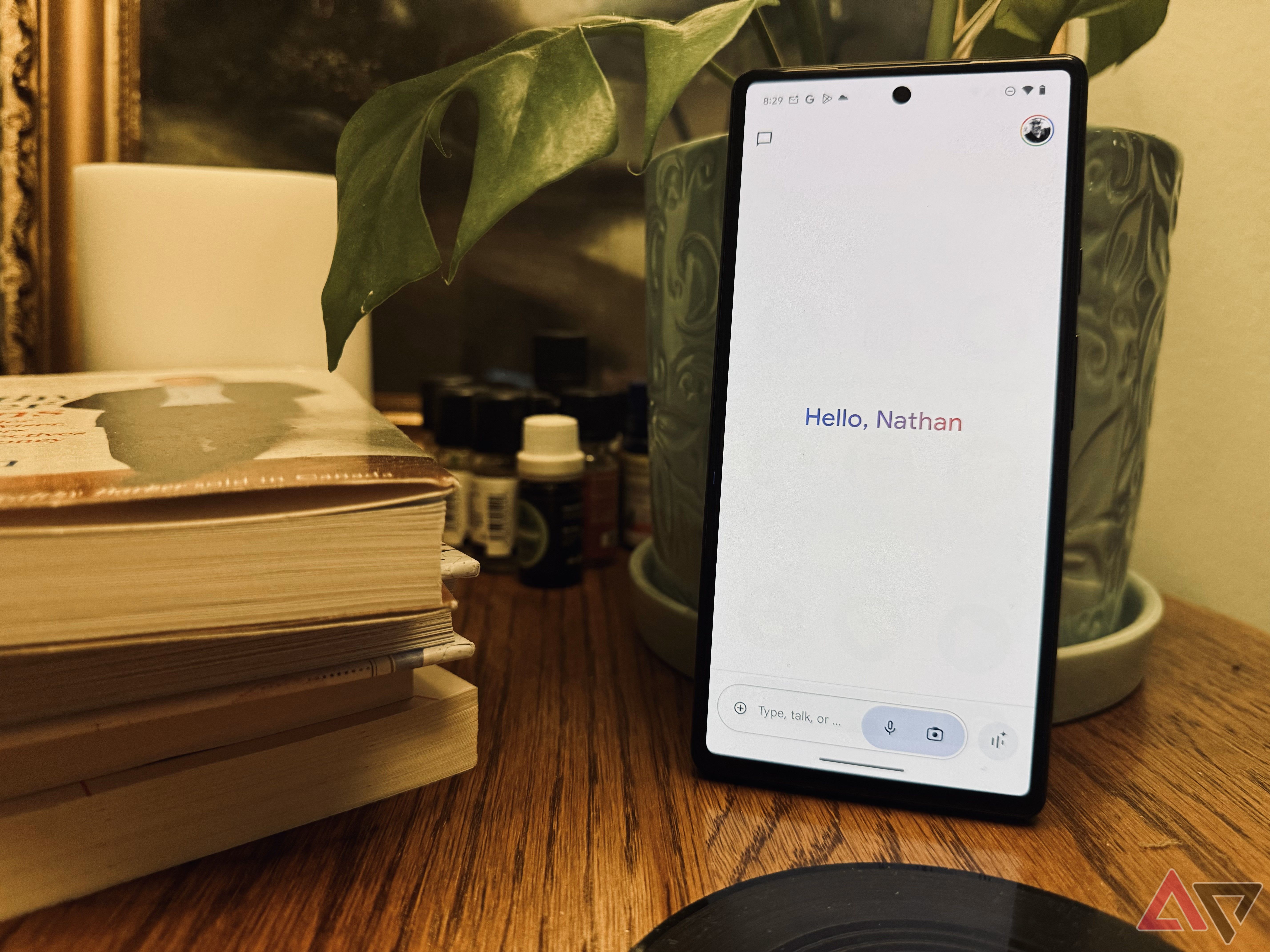 Google Gemini's new interface on a Pixel 6 on a table with a plant in the background and a stack of books nearby.