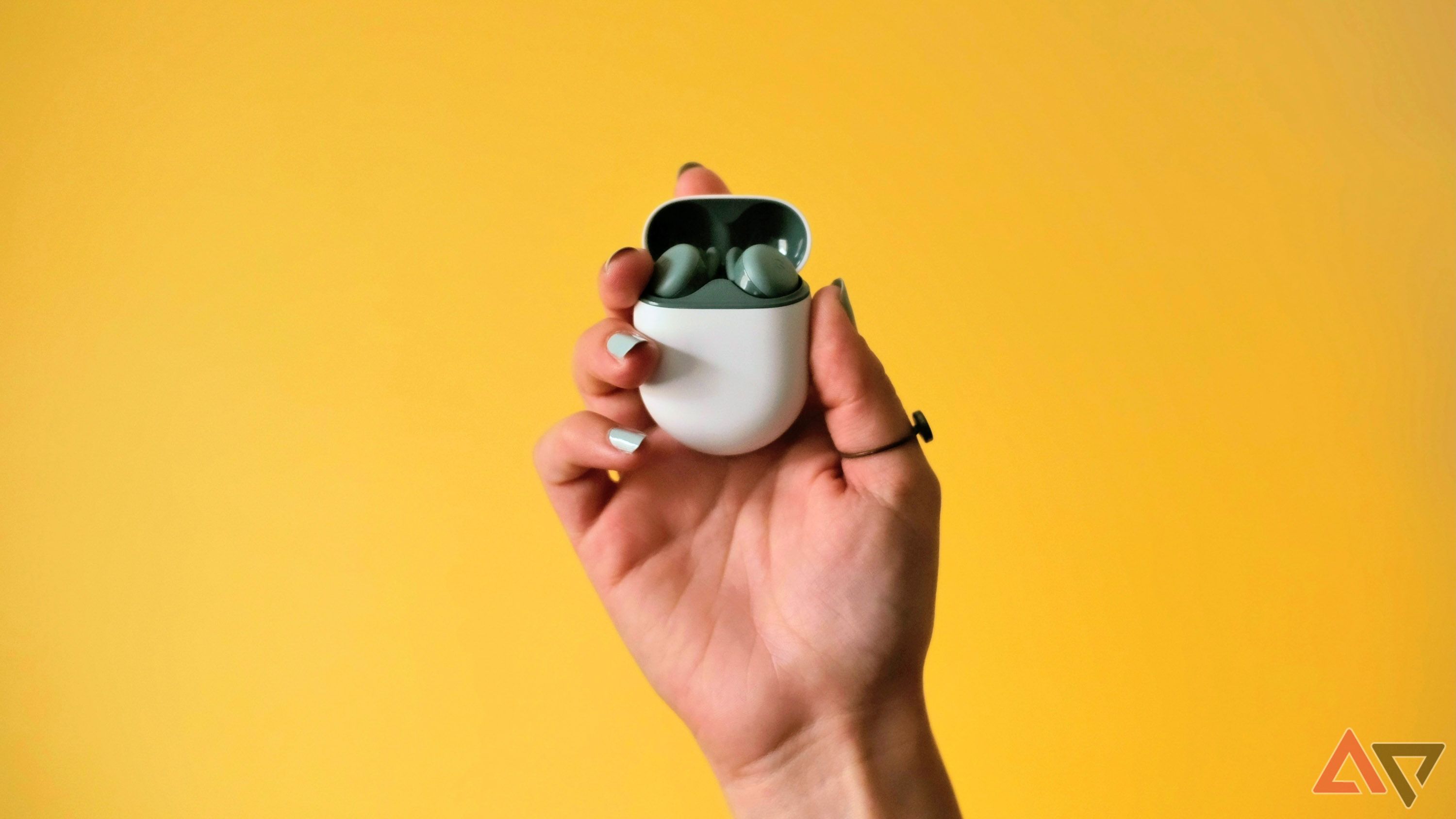 The Pixel Buds A-Series in a woman's hand in front of a yellow background.