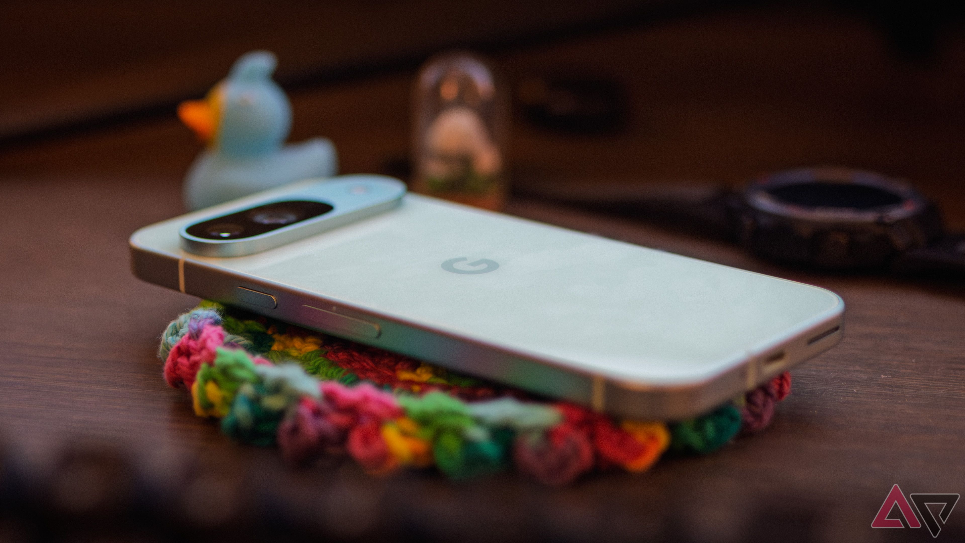 The Google Pixel 9 rear-side up on a colorful coaster on a wooden desk.