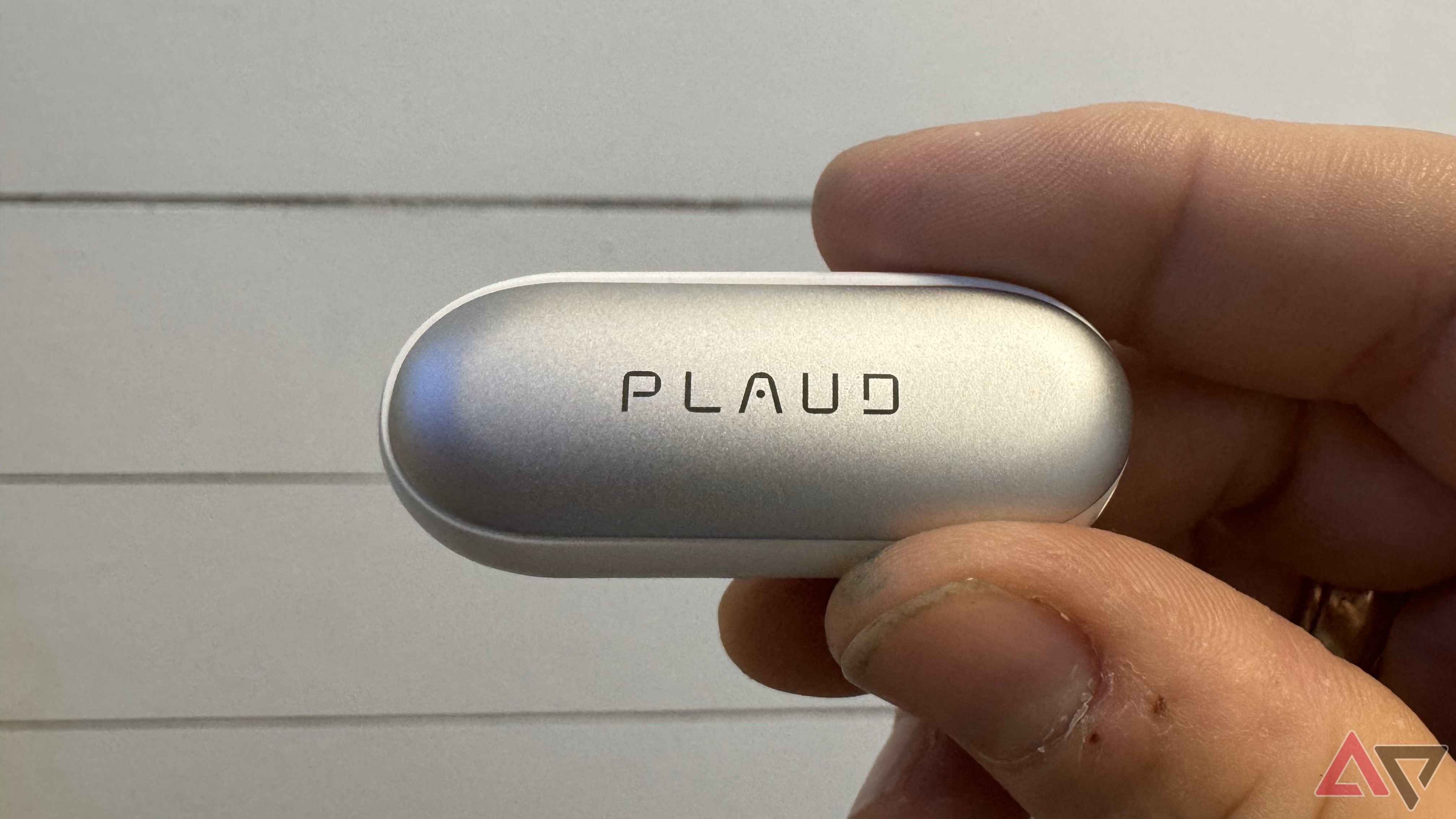 Plaud logo on the back of a memo pin held up in front of a white wall