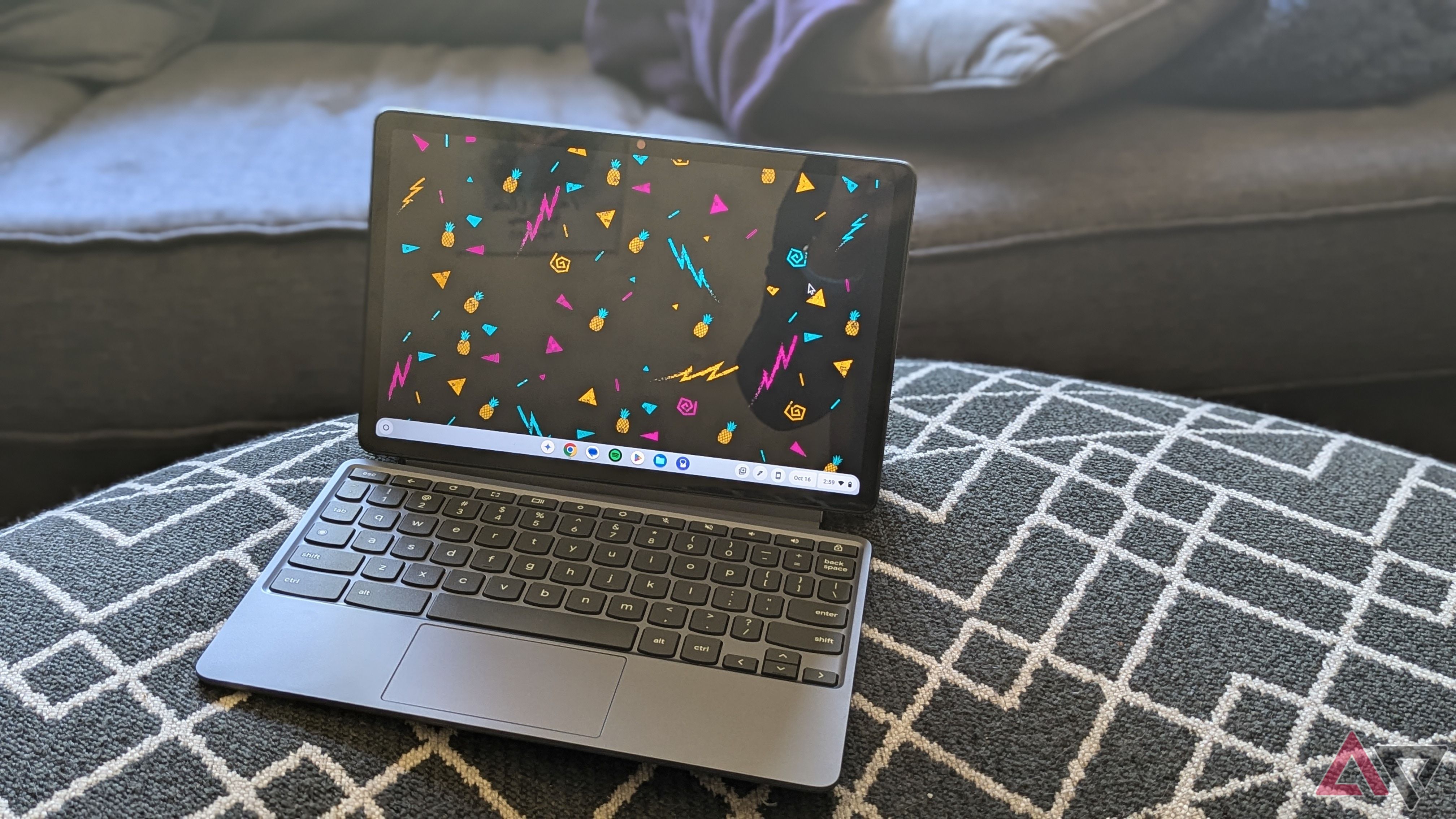 Lenovo Chromebook Duet 11 (2024) with pineapple background sitting on a black ottoman with white pattern in front of a blue sofa