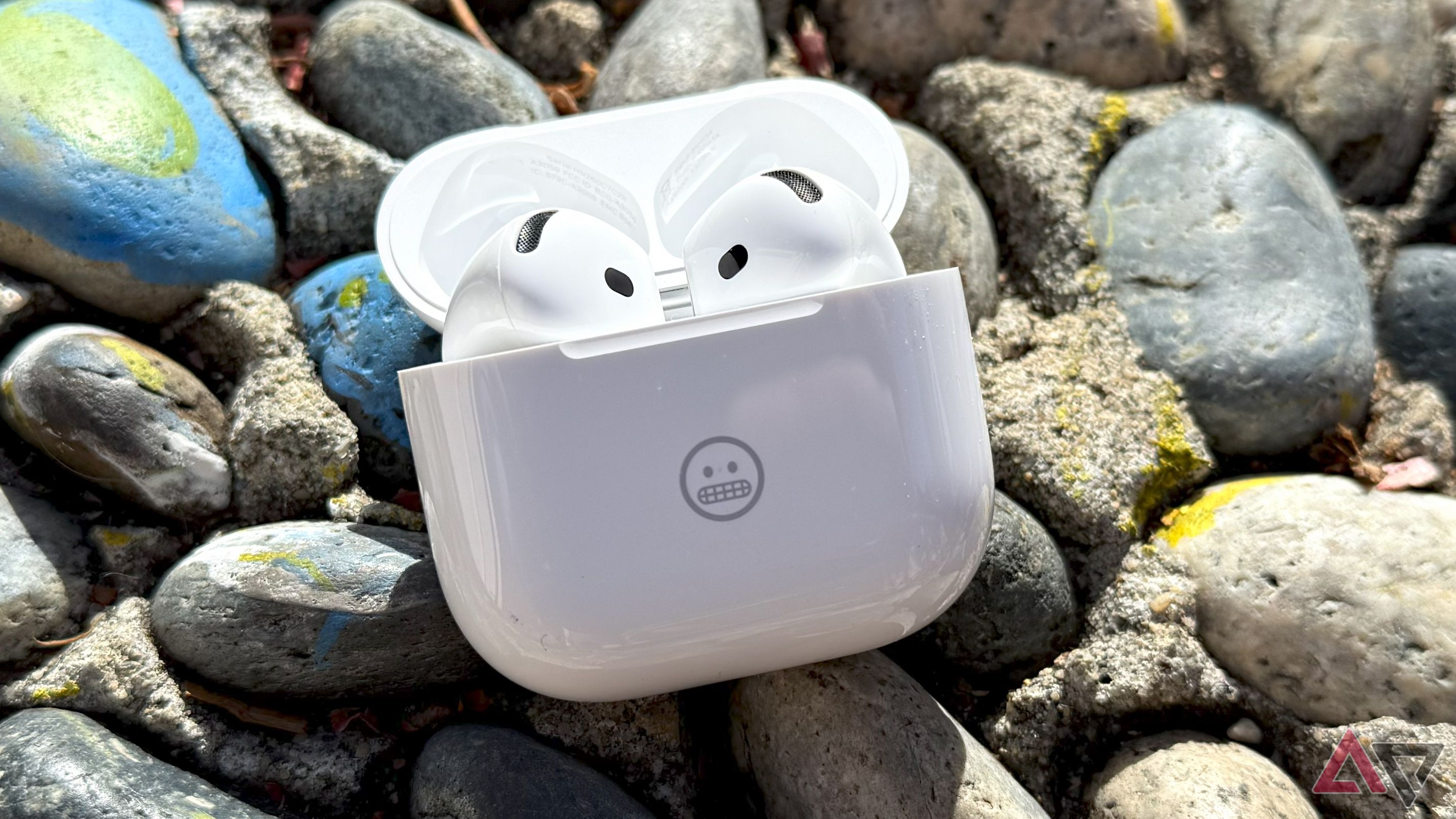 AirPods 4 earpods in their charging case lying on rocks