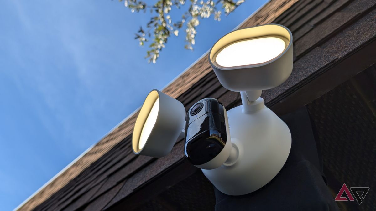 Arlo Wired Floodlight Camera under overhang with roof and tree in background with lights on