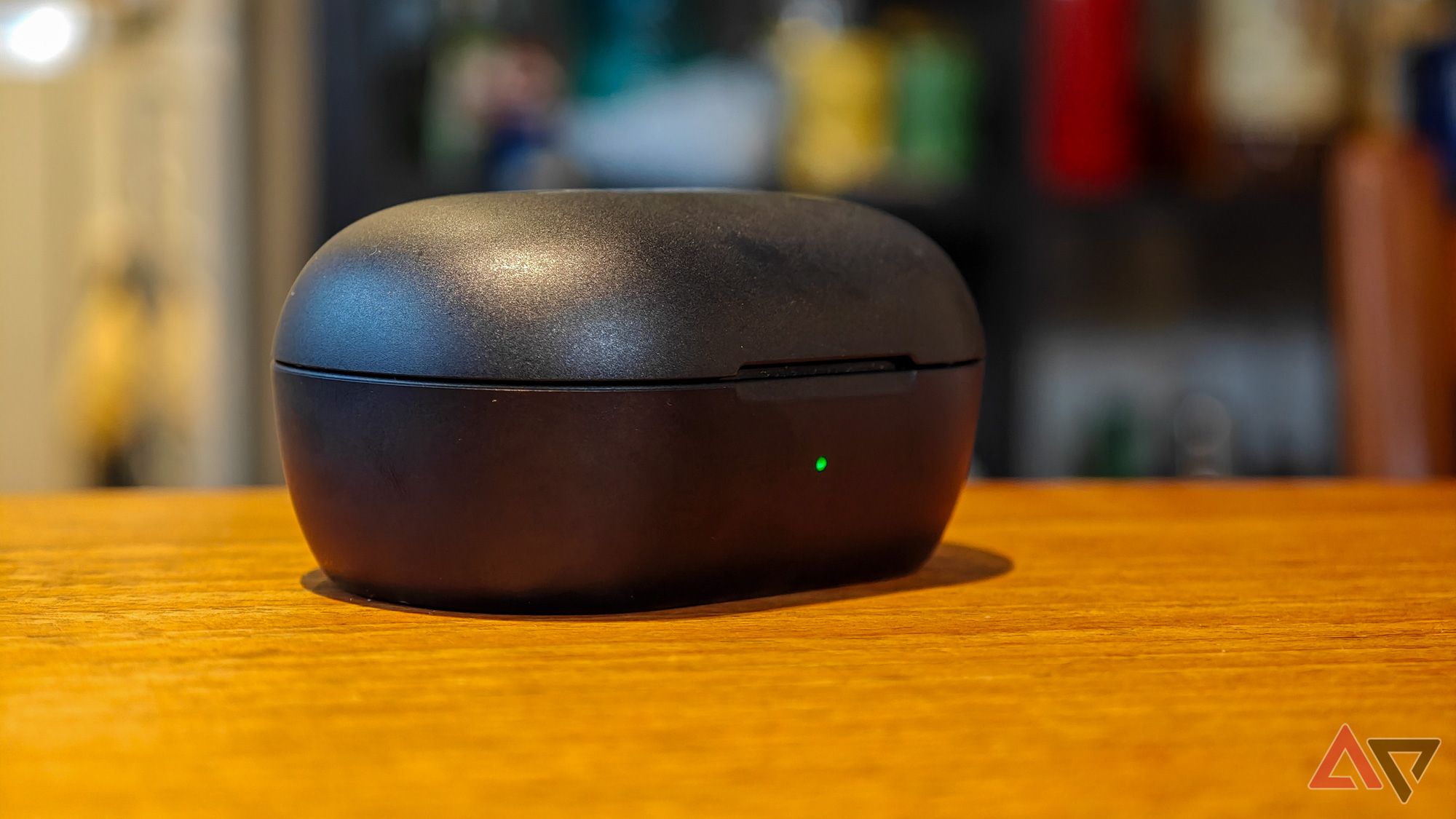 Bose QuietComfort Earbuds case on a wooden table with a green power LED