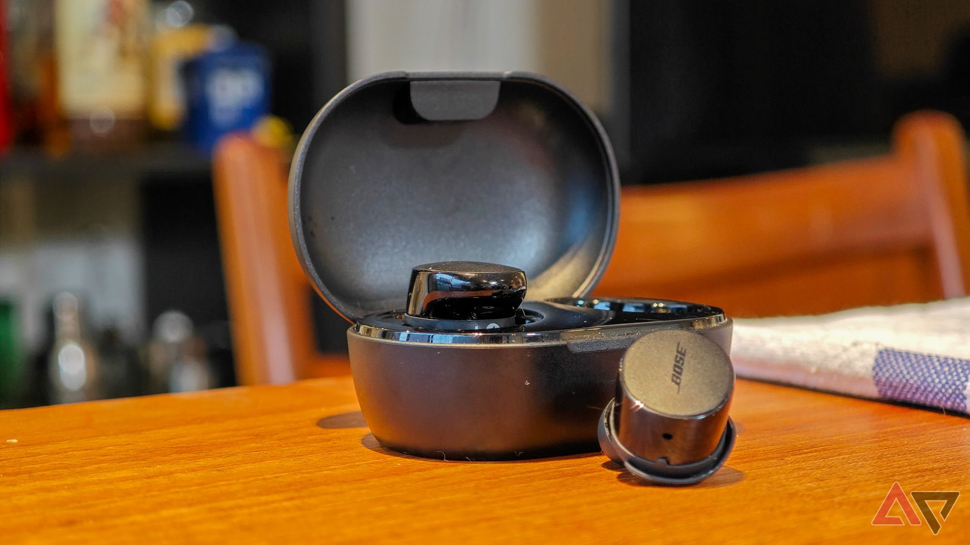 Bose QuietComfort Earbuds sitting on a wooden table with one ear outside