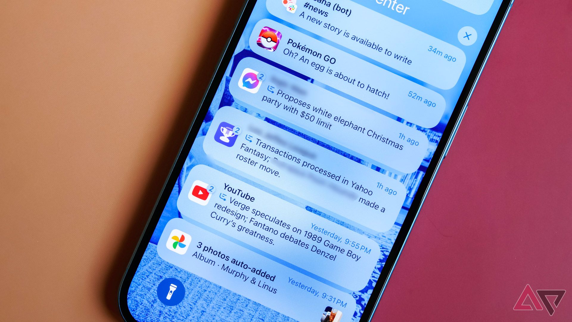 An iPhone 16 against a colored backdrop with numerous notification summaries on screen.