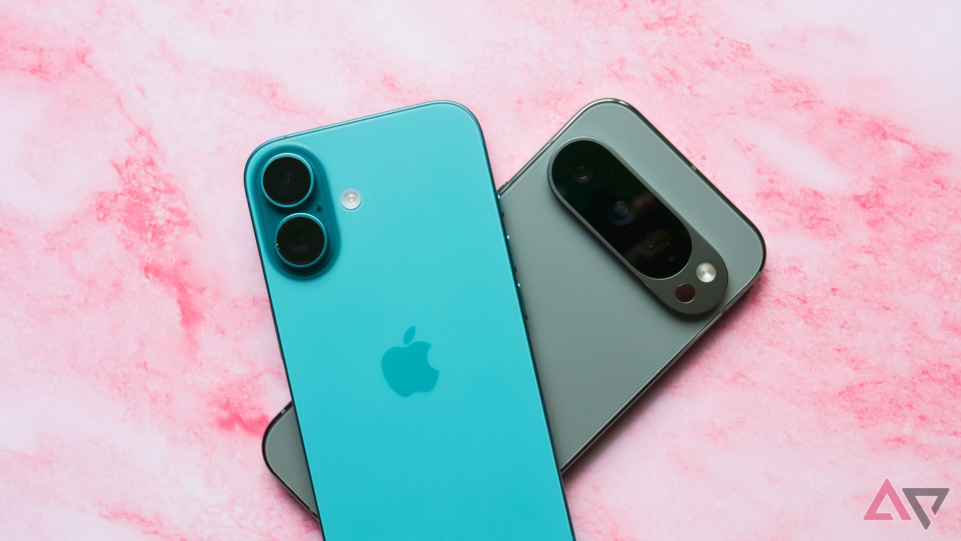 An iPhone 16 lying on top of a Pixel 9 Pro on a pink backdrop.