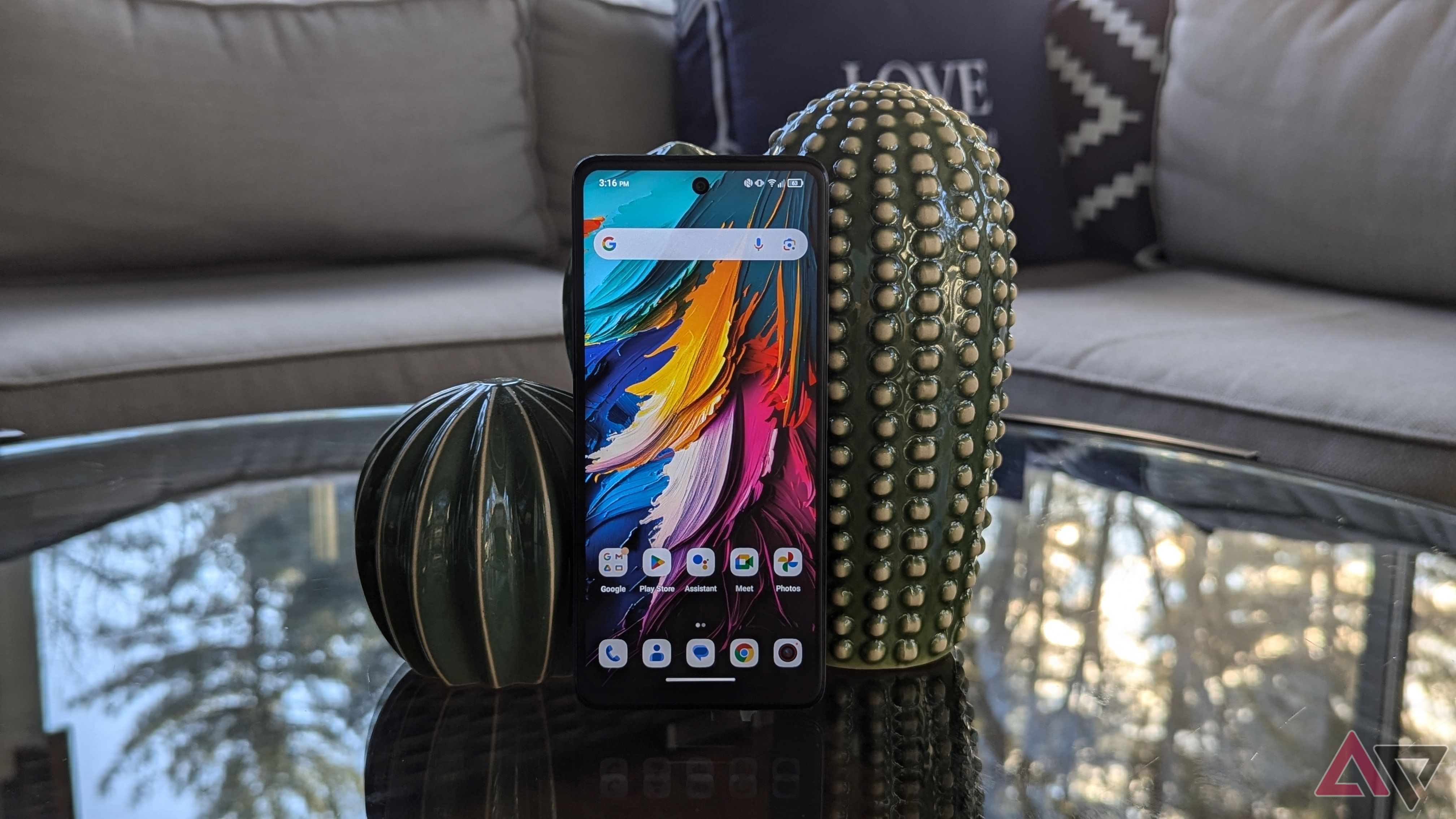 A TCL 50 XE NXTPAPER 5G phone leaning against some ceramic cacti on a glass table in front of a grey couch