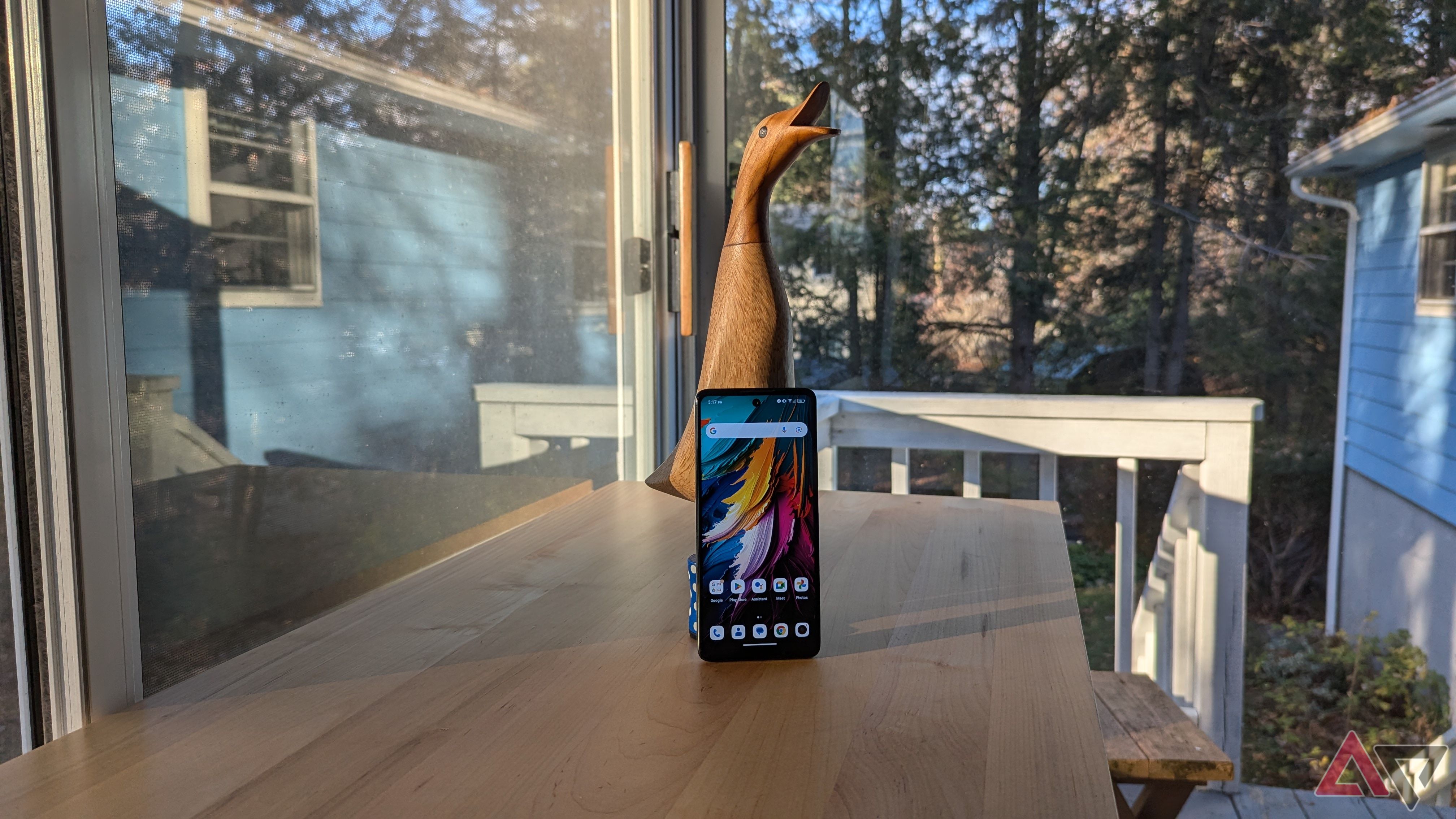 A TCL 50 XE NXTPAPER 5G propped up on a wooden goose on top of a wooden table in front of some windows