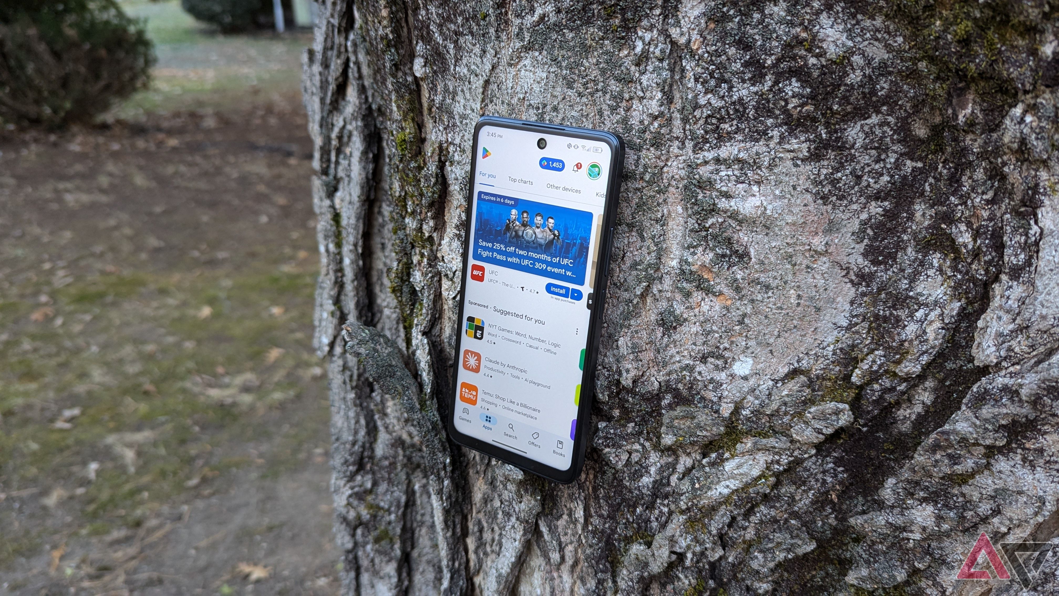 A TCL 50 XE NXTPAPER 5G perched on a tree with the screen visible and the Google Play Store open