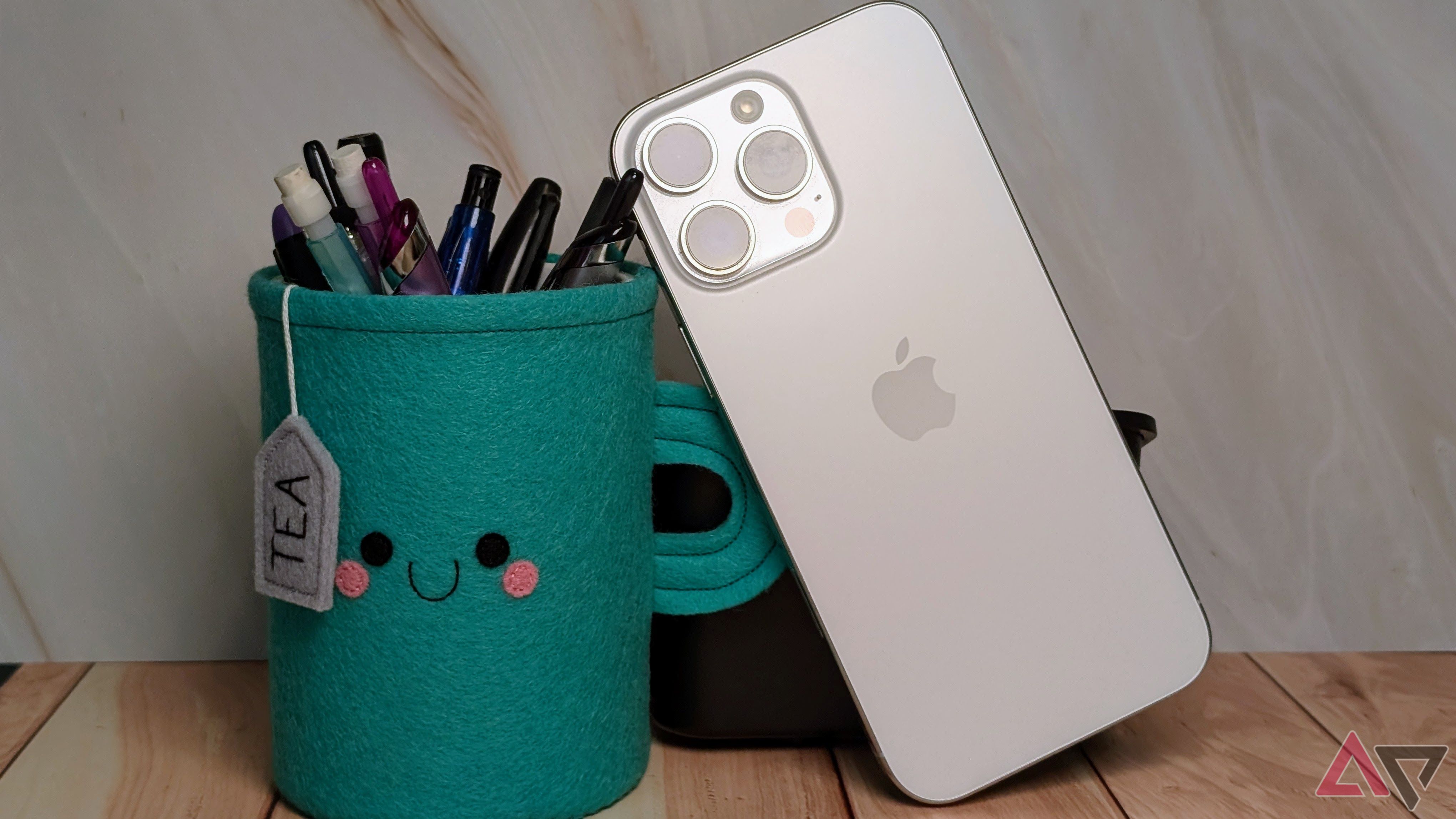 The iPhone 16 Pro next to a teal felt tea cup with pens and pencils